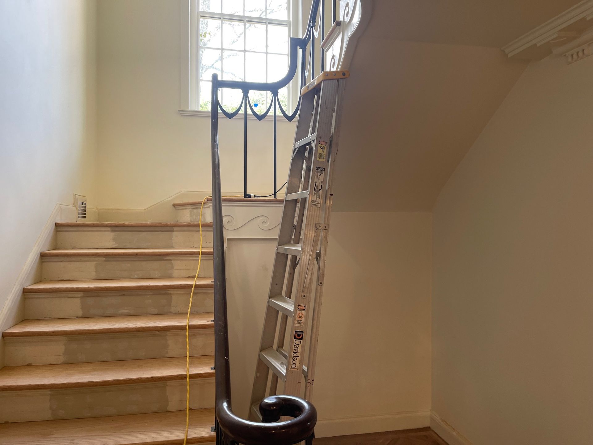 Ladder leaning against a staircase with a window.