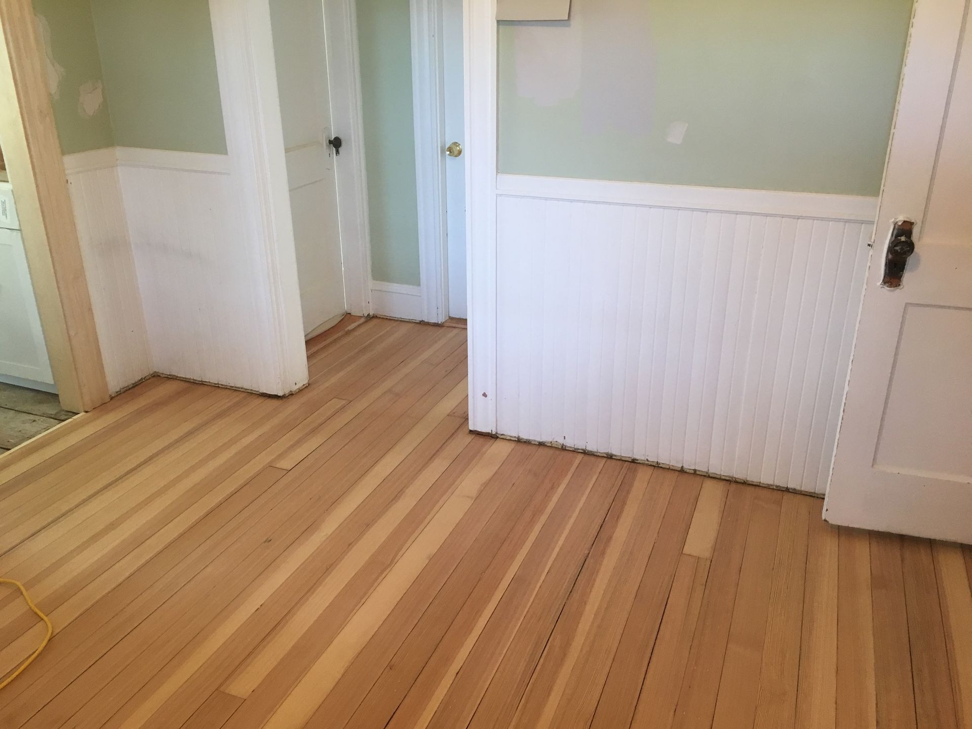 Newly refinished wood floor in a room with white wainscoting and light green walls.