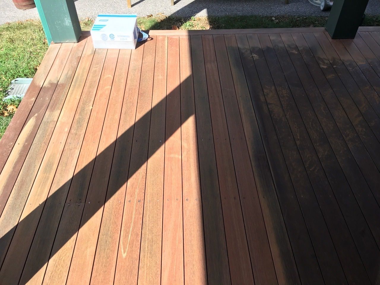Wooden deck, half stained dark brown, half unstained, under a bright sunlight.