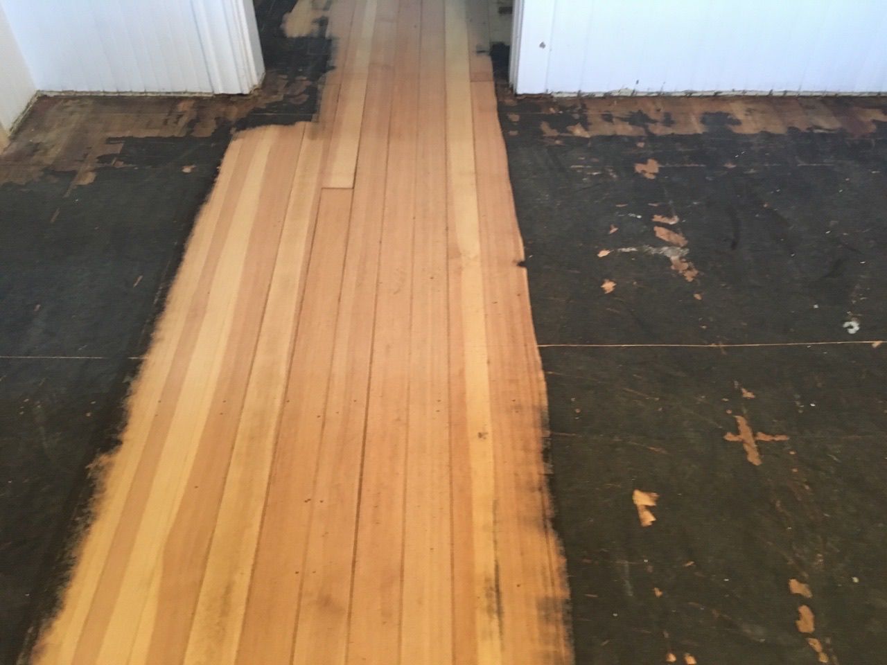 Wooden floor partially stripped of black paint, revealing the natural wood color.