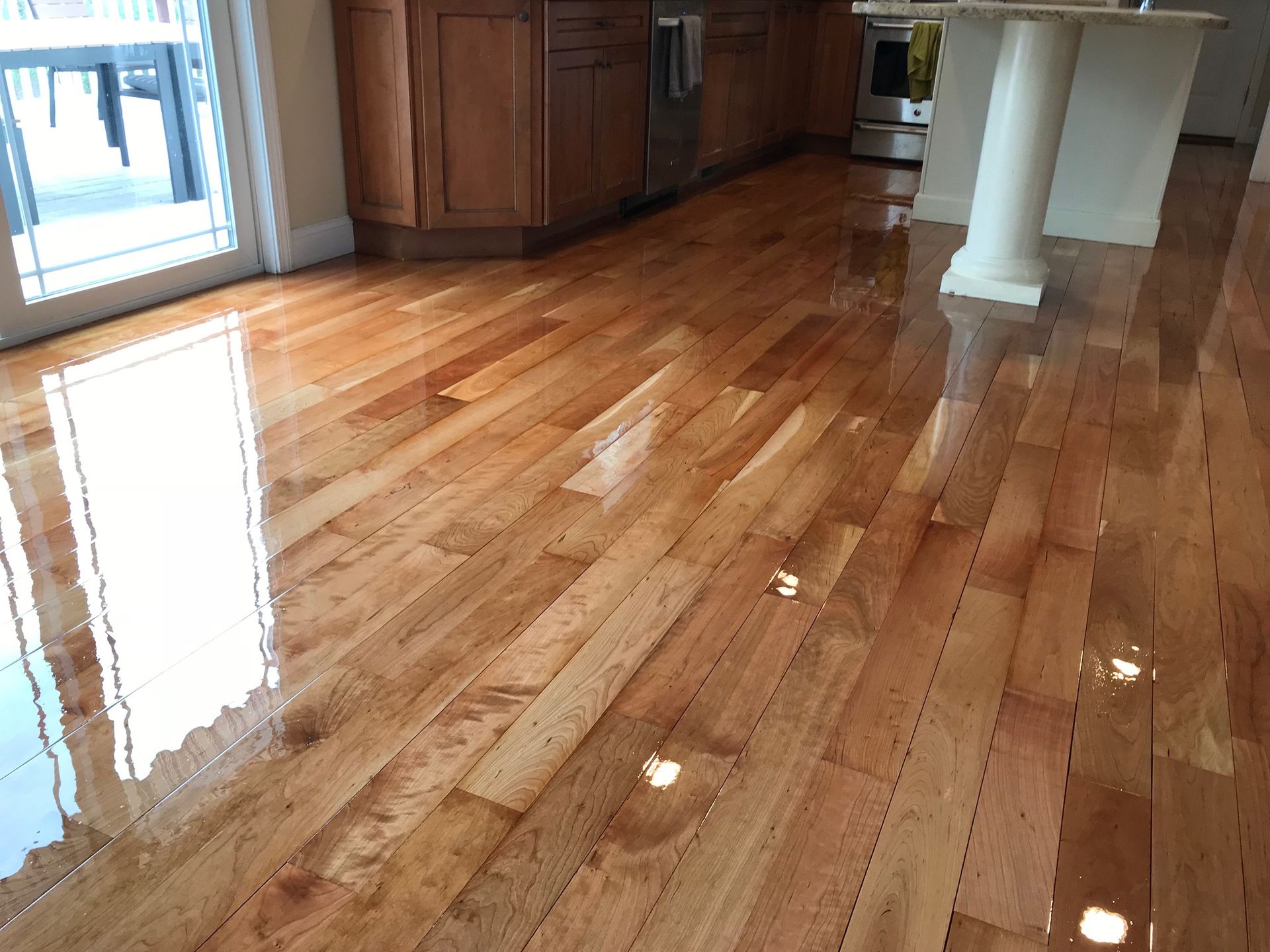 Reflected light on shiny, medium-brown hardwood floors in a kitchen with wooden cabinets and a white island.