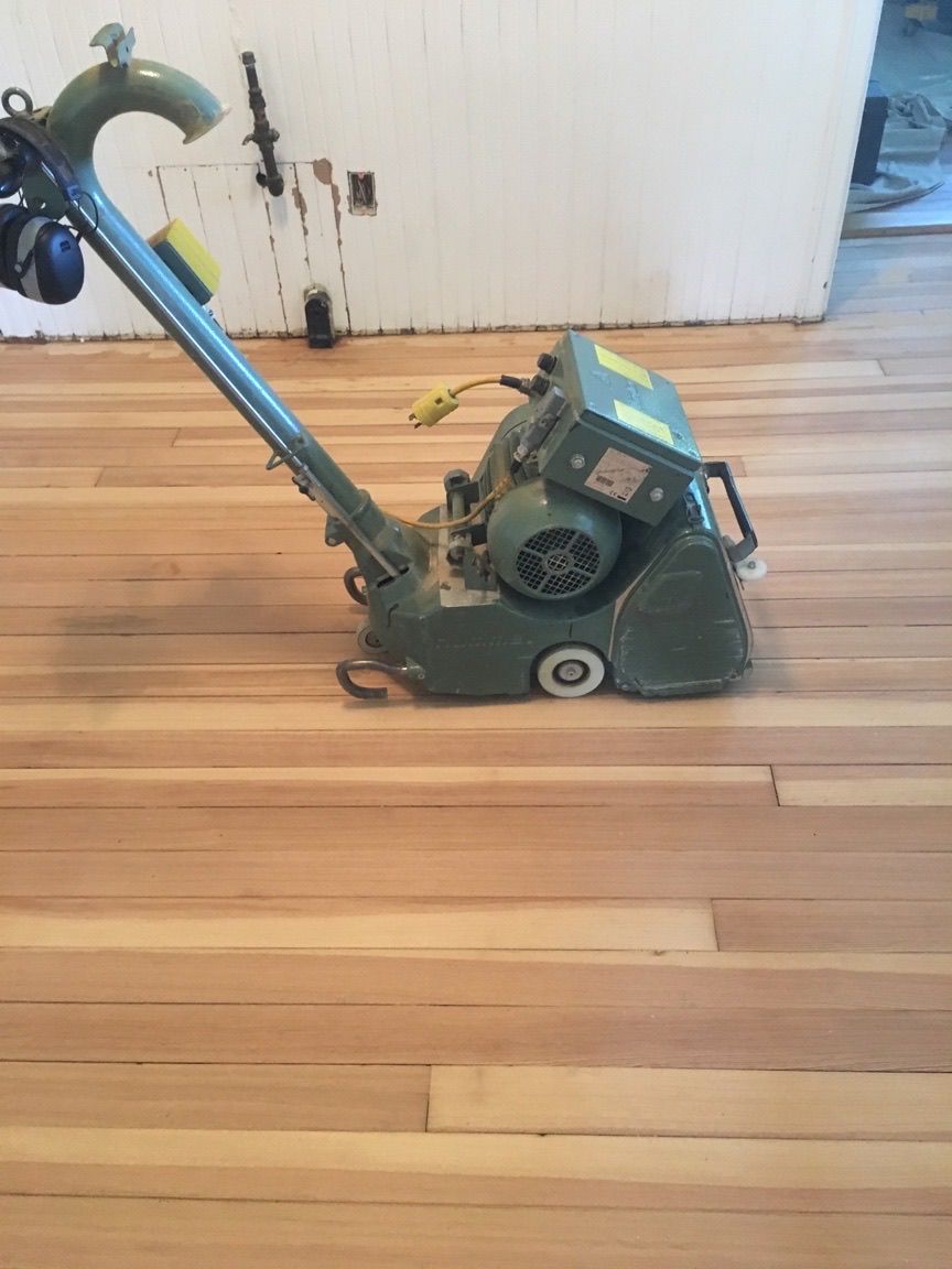 Floor sander on light wood floor. Green machine, yellow cord.
