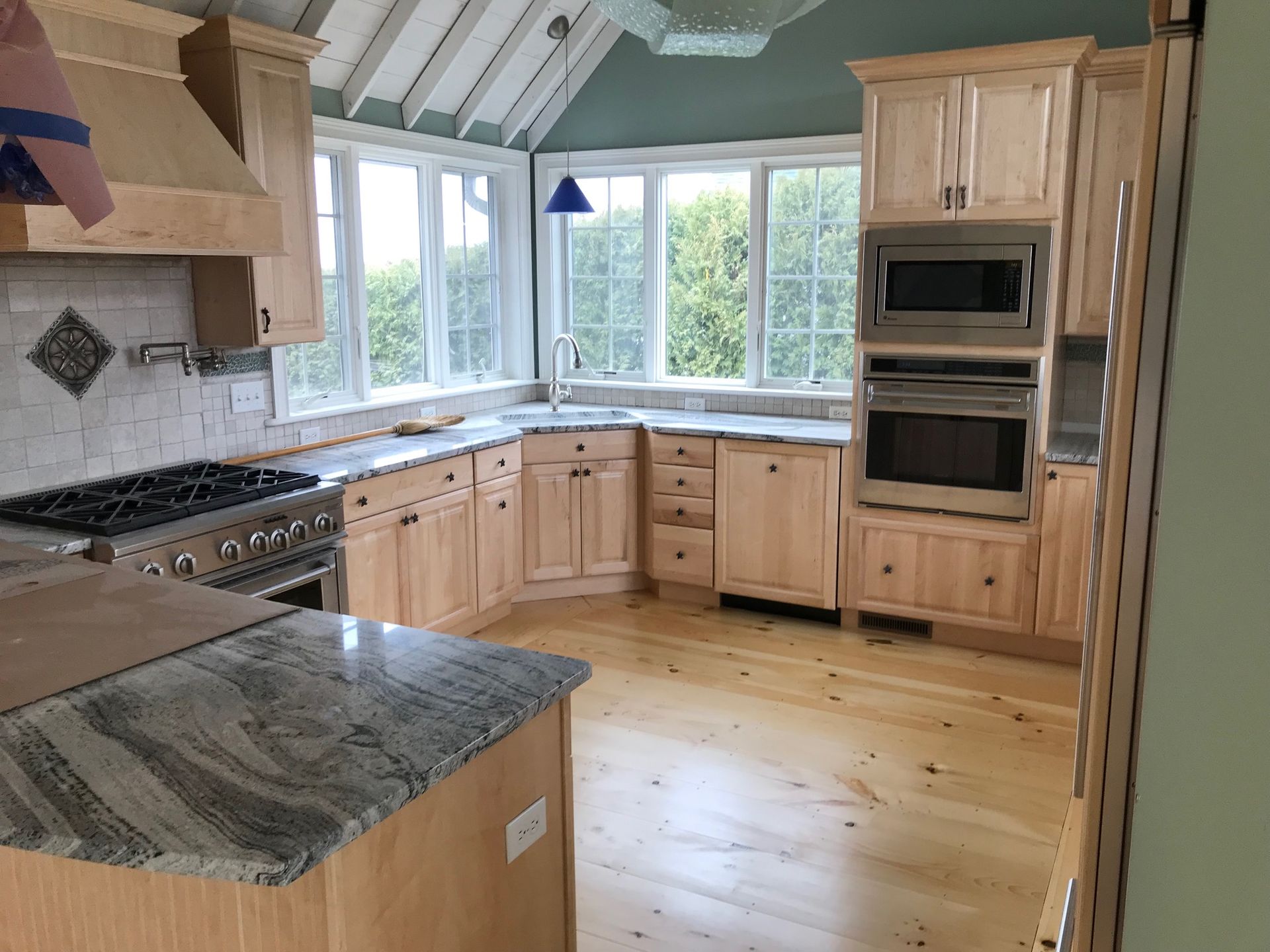 Light wood kitchen with granite countertops, stainless steel appliances, and a window corner.