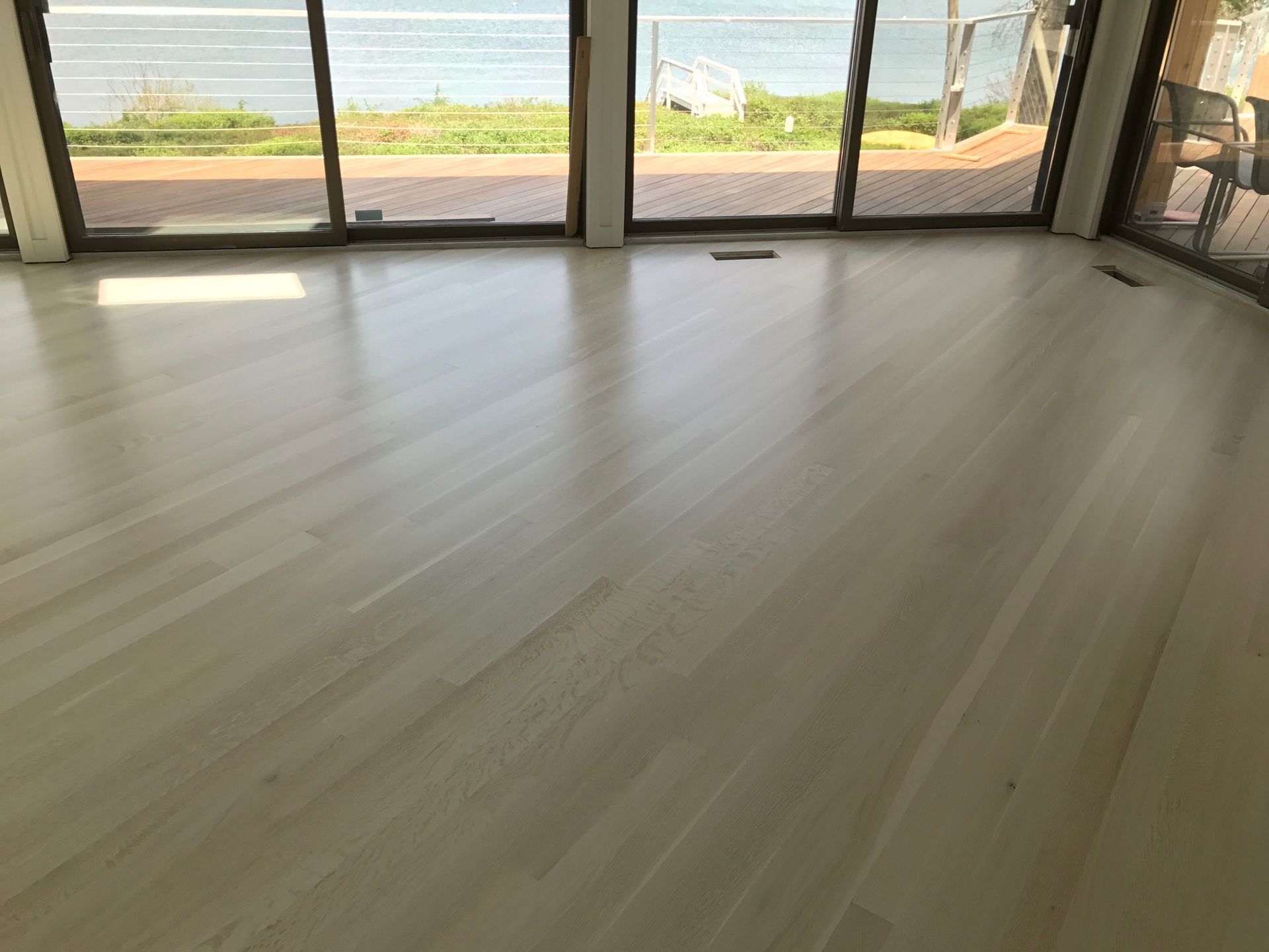 Light-colored, glossy wooden floor in a bright room with large windows overlooking a body of water.