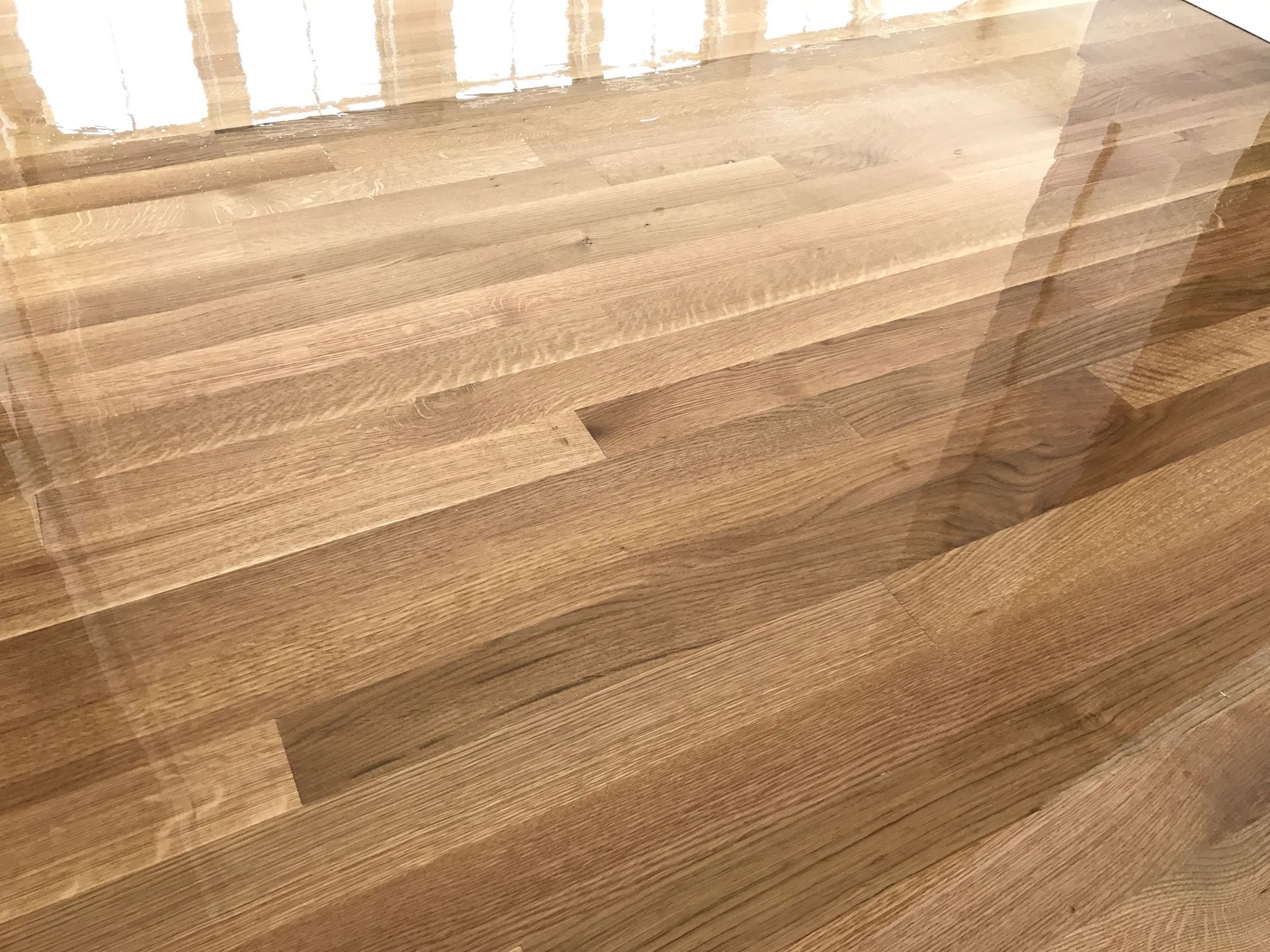 Shiny, light-brown wooden floor reflecting light, probably in a room with windows.