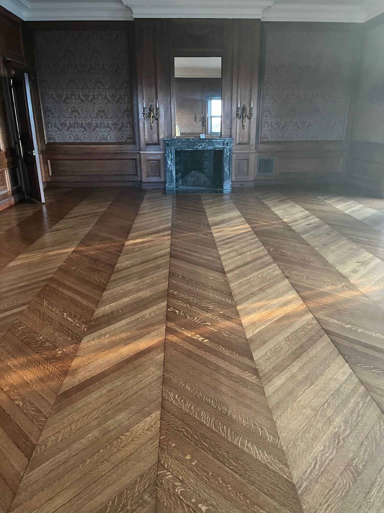 Wooden floor with angled pattern in a room with a fireplace, mirror, and decorative wall panels.