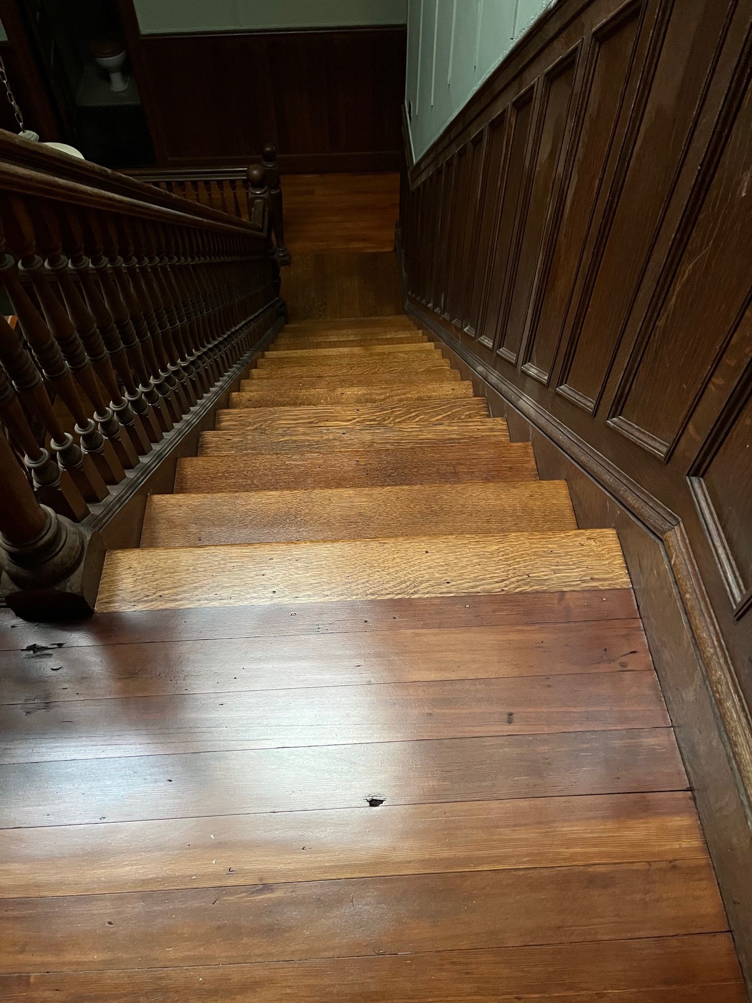 Wooden staircase, dark brown, viewed from above. Banister on the left, paneling on the right.