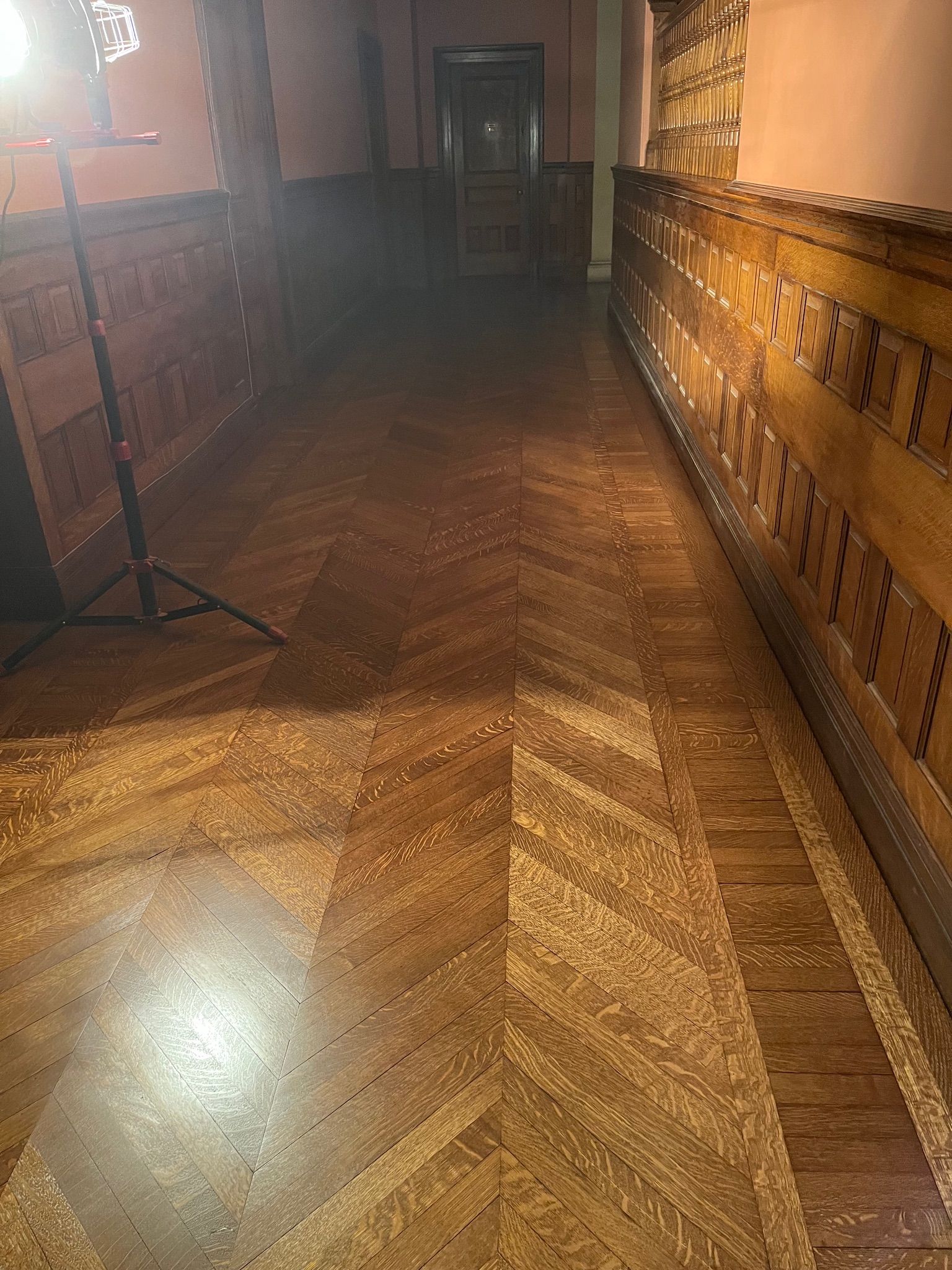 Long hallway with wood paneling, parquet floor, and a door at the end.