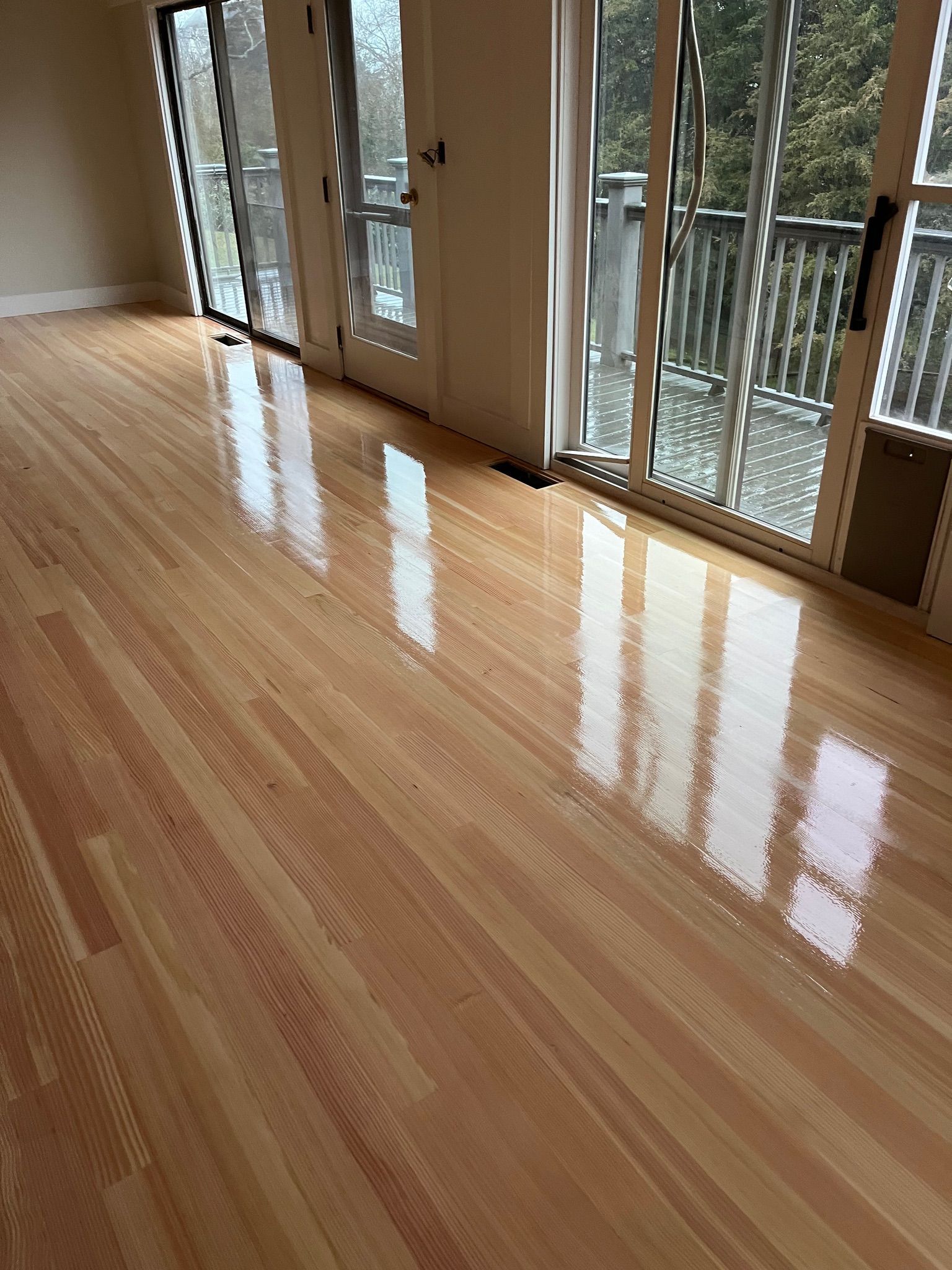 Shiny hardwood floor in room with glass doors to a deck, reflecting light.