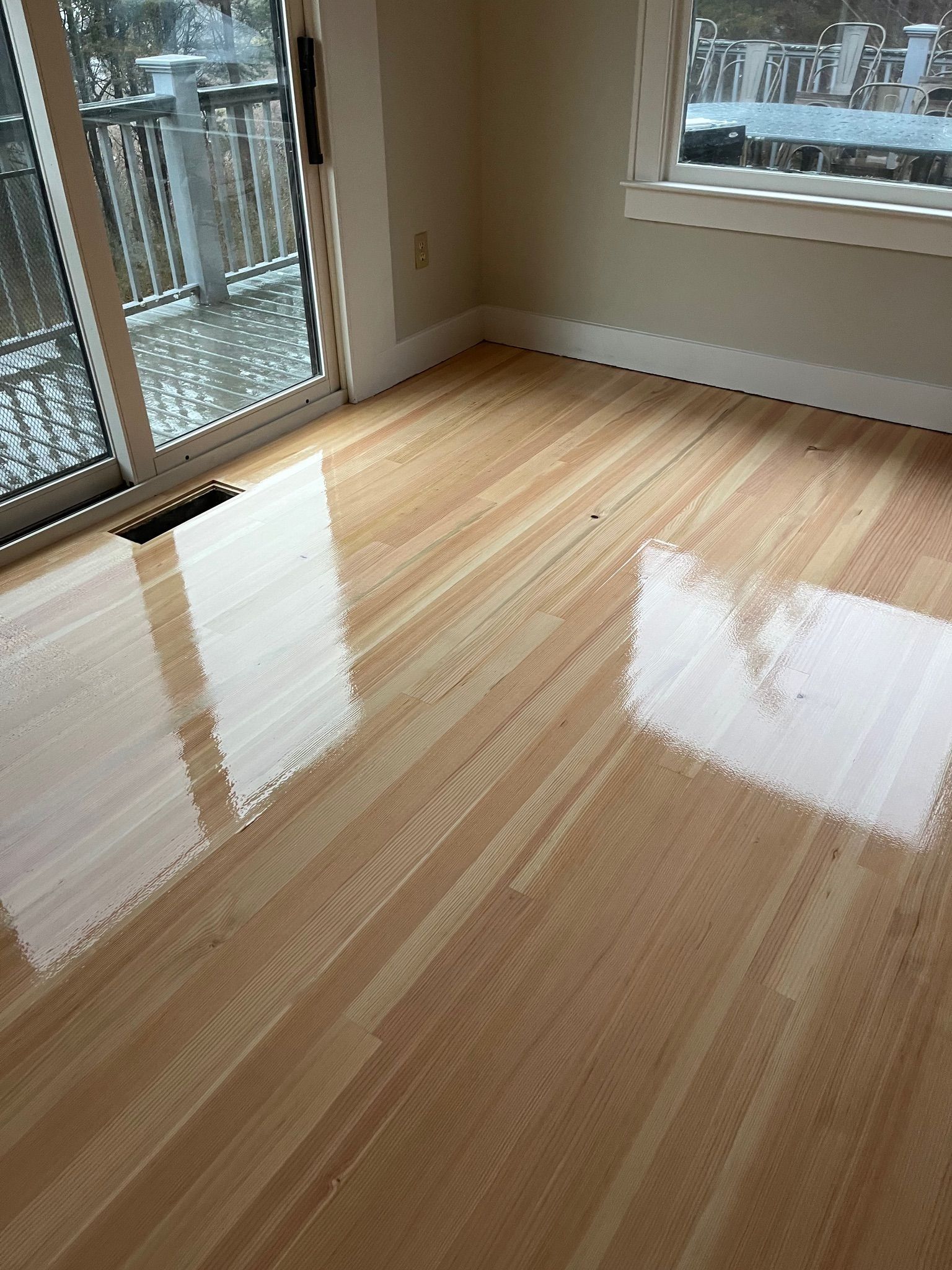 Shiny, light-colored wood floor partially covered with white substance, next to a sliding door leading to a deck.