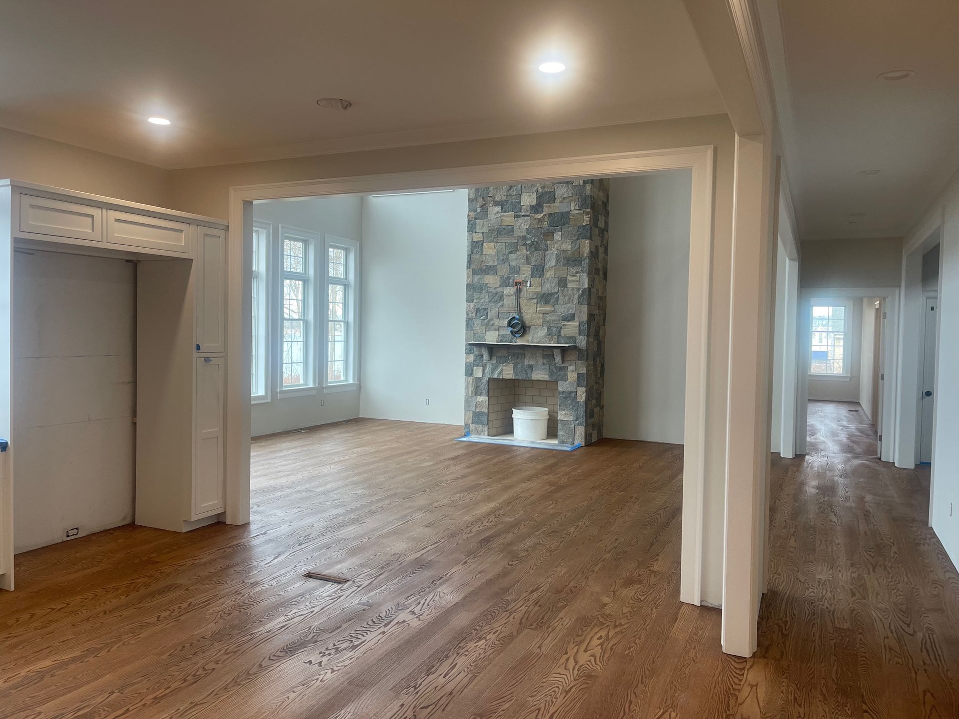 Interior view of a room with hardwood floors, stone fireplace, and white trim. Hallway visible on right.