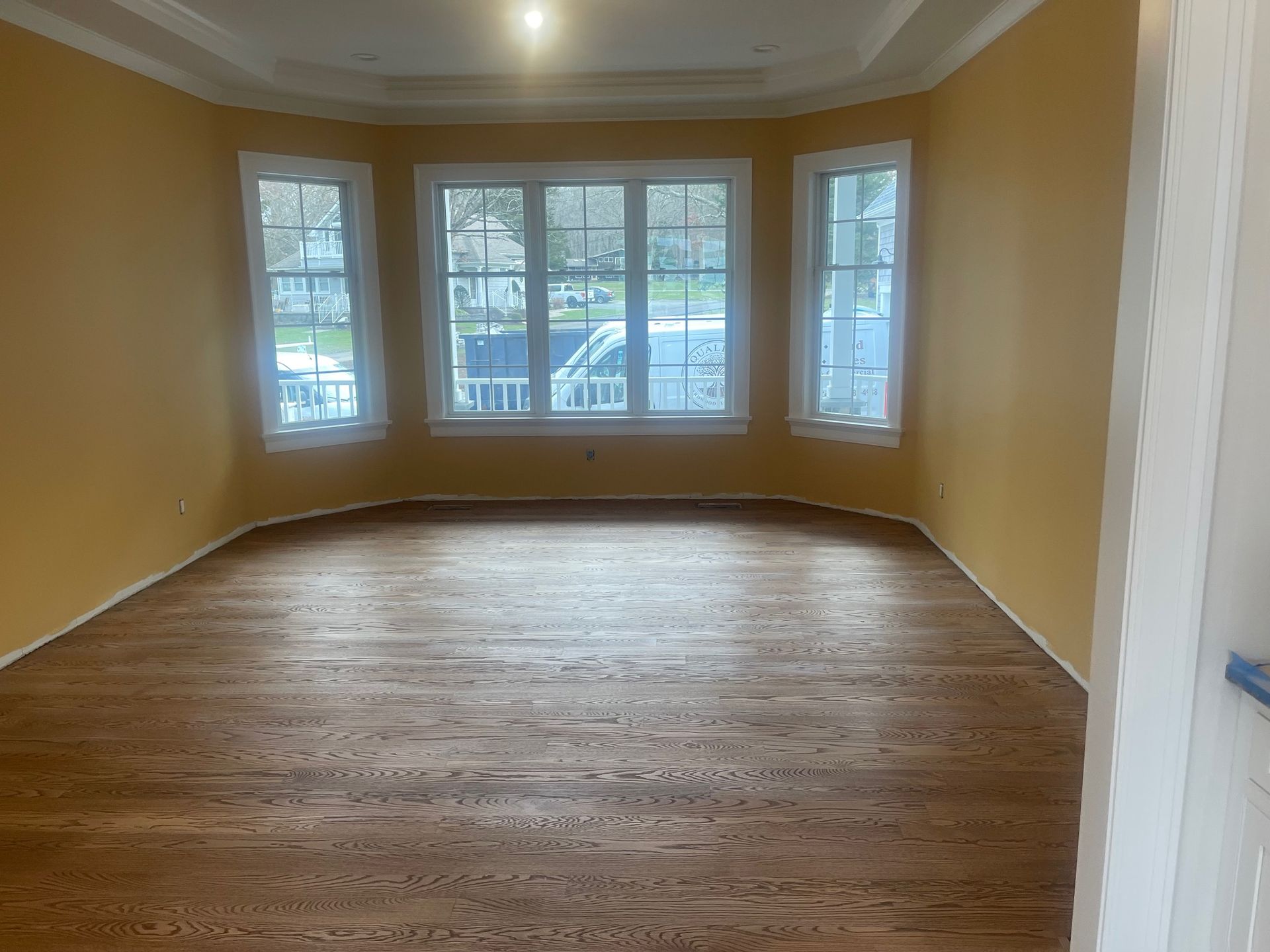Empty room with hardwood floors, bay window, and yellow walls.