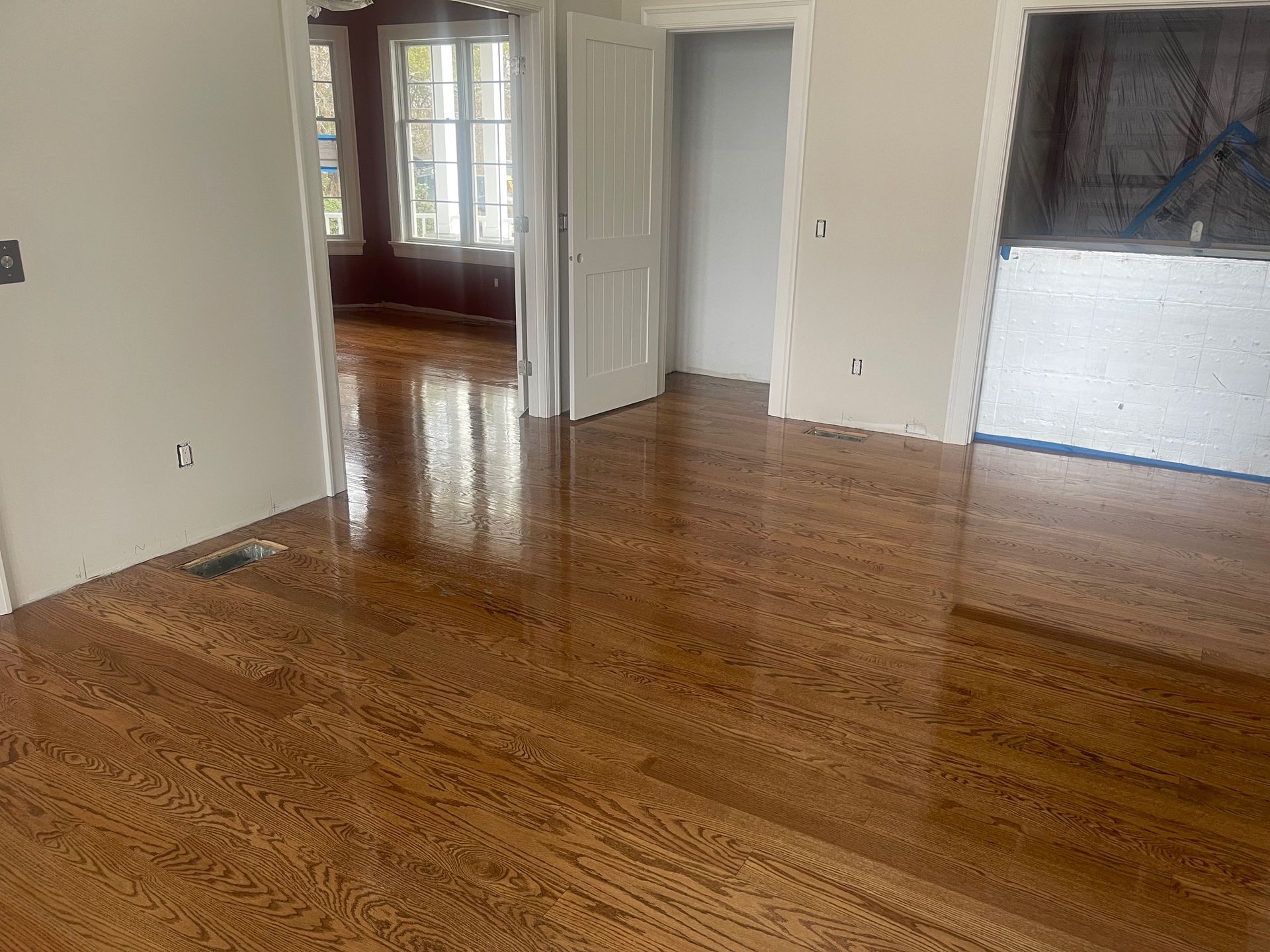 Shiny hardwood floor in a room with white walls, an open doorway to another room, and a doorway to a unfinished room.