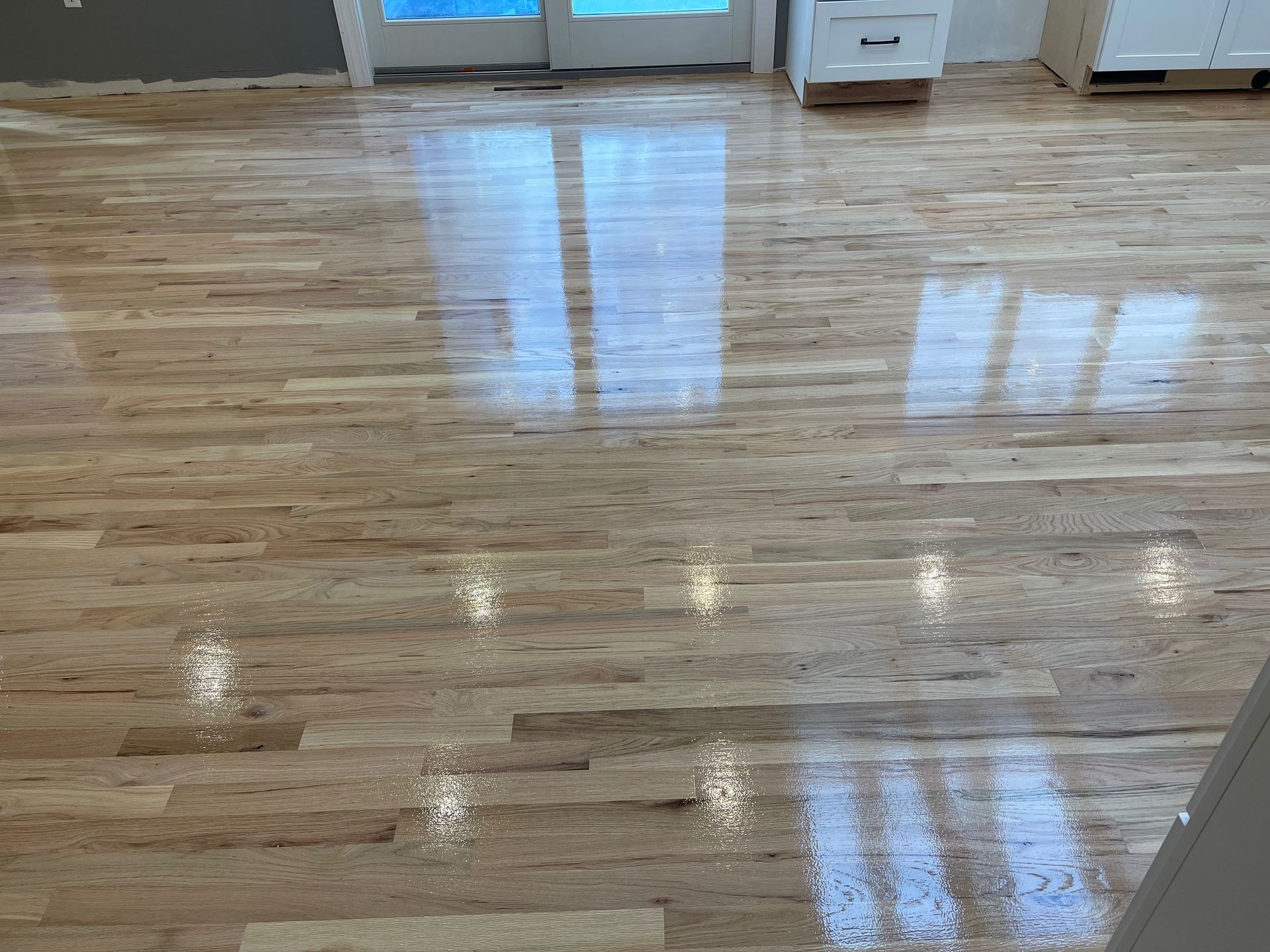 Reflective hardwood floor with natural wood tones. Light from a window reflects on the surface.