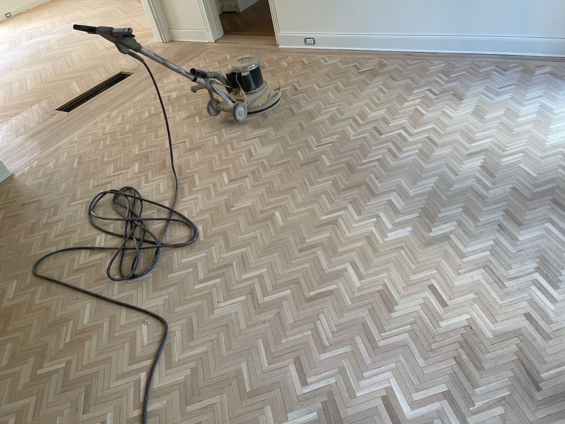 Floor sander on herringbone patterned wood floor, sanding and refinishing.