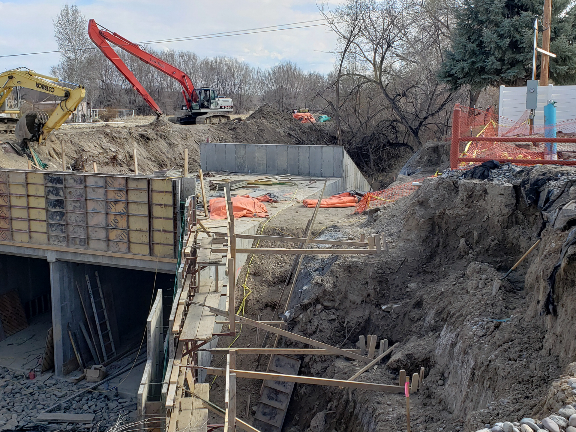 Construction site with excavators, exposed earth, concrete forms, and a tunnel entrance.
