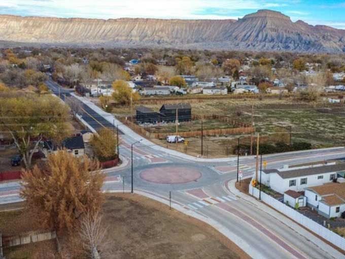 Rural town intersection with roads, scattered homes, fields, and mountains in the background.