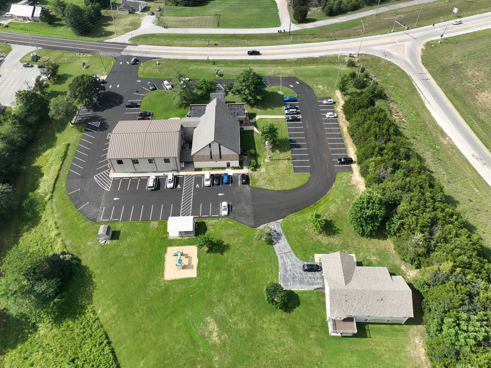 Aerial view of a small church with parking lot, grassy grounds, and a separate building nearby.