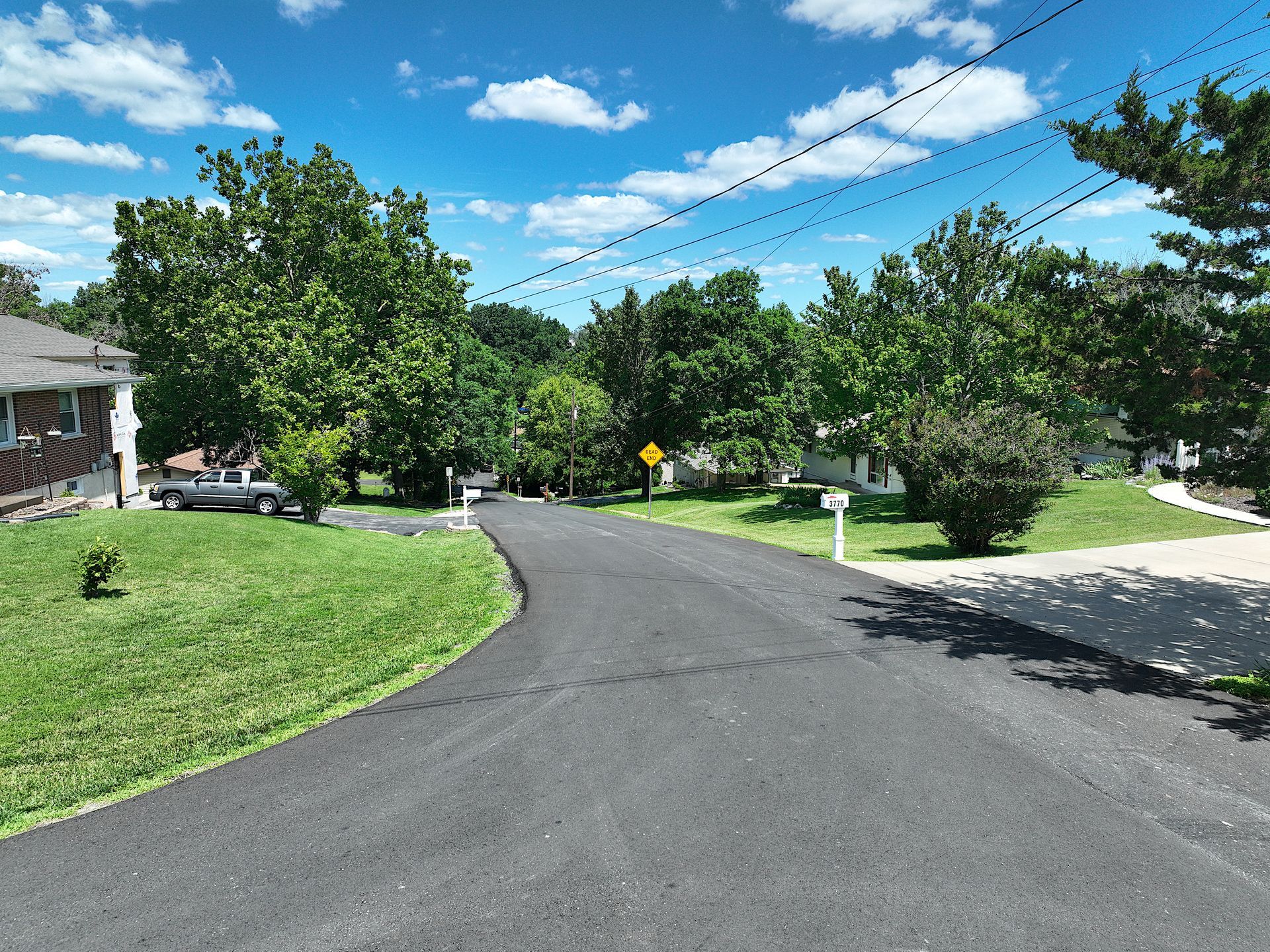 Curved suburban street with green lawns, trees, and a bright blue sky