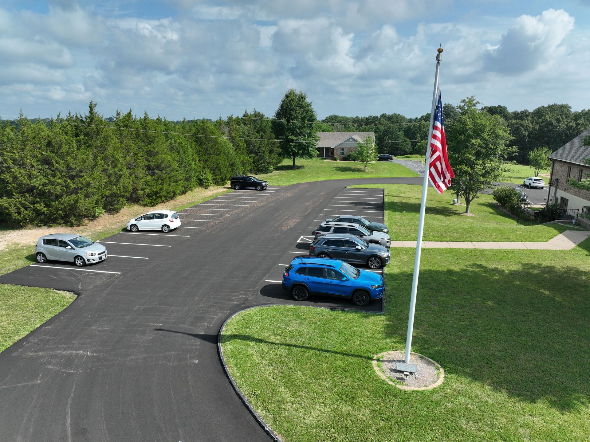 Aerial view of a parking lot with several cars and an American flag on a grassy median.