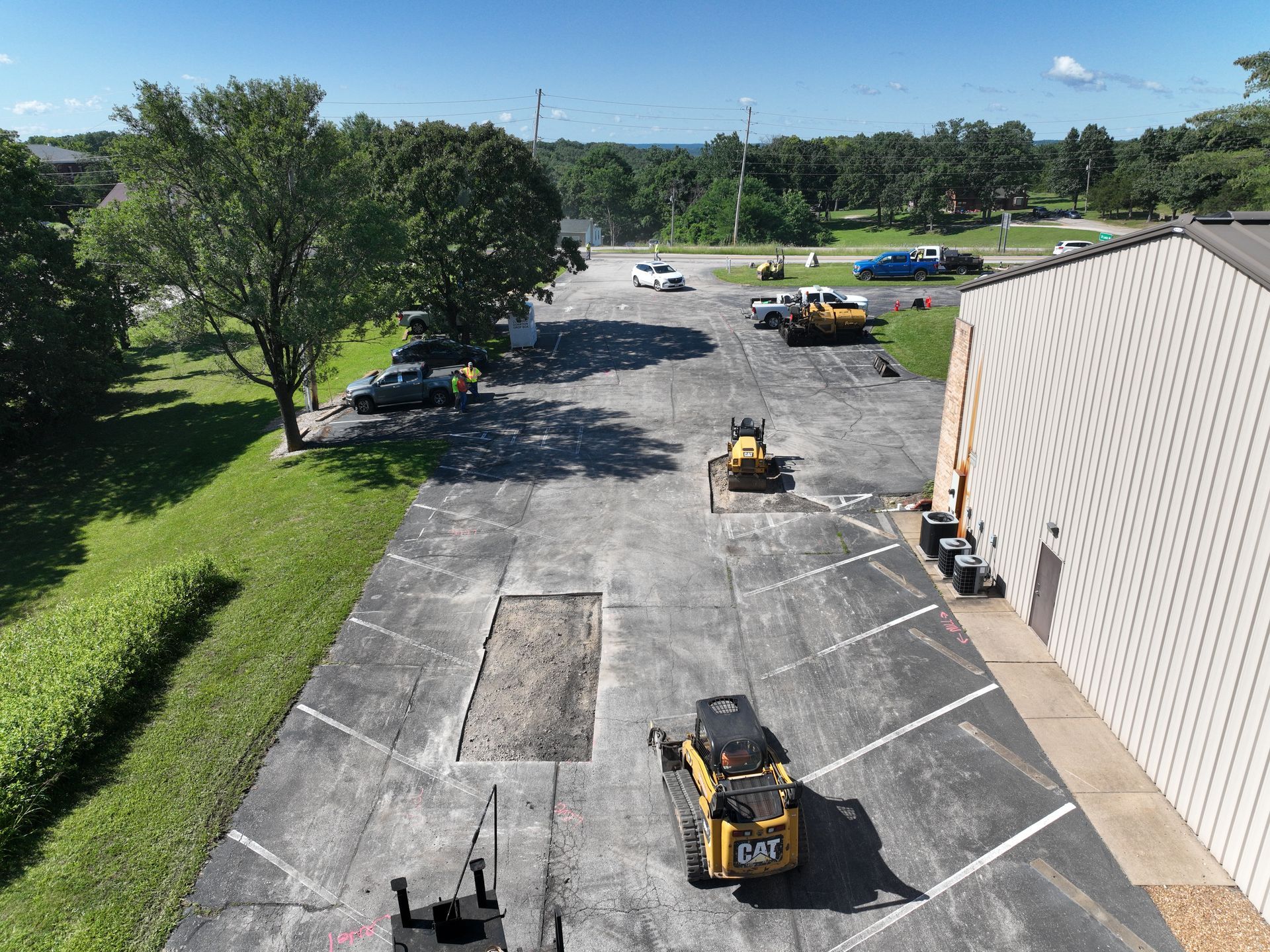 Parking lot with construction equipment and workers near a beige building on a sunny day