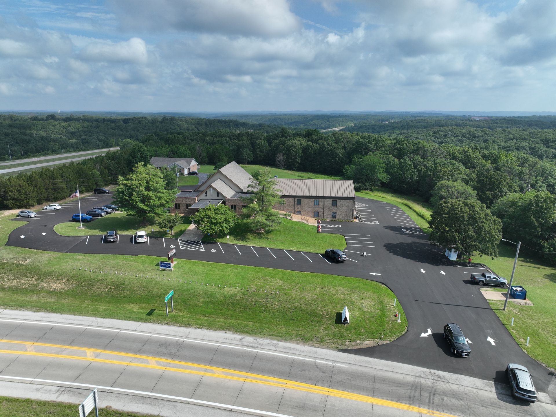 Aerial view of a building complex with parking lot, surrounded by trees and grassy grounds.