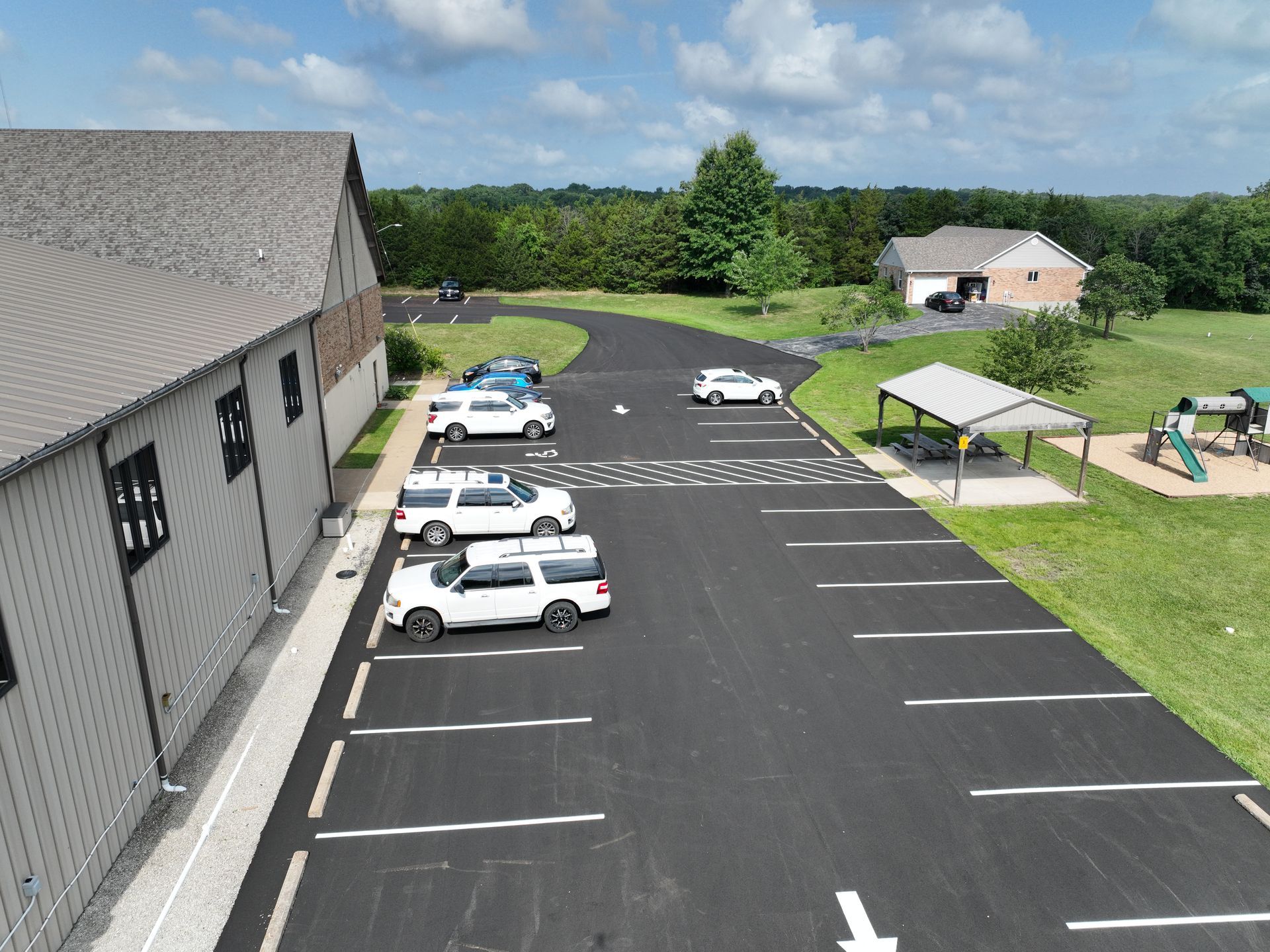 Parking lot beside a gray building with several parked cars and a picnic shelter on a sunny day