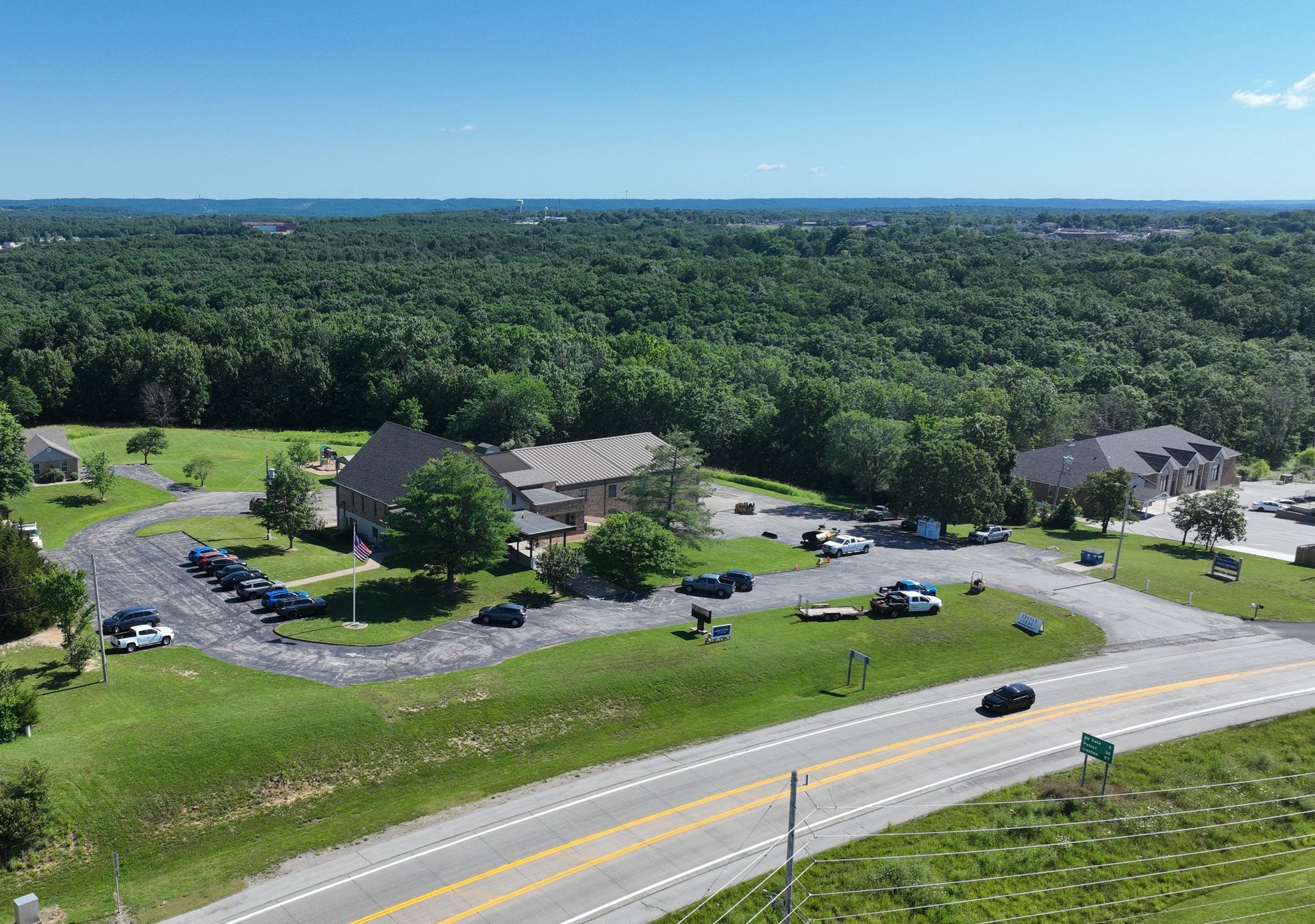 Aerial view of a suburban apartment complex beside a highway, surrounded by dense green trees