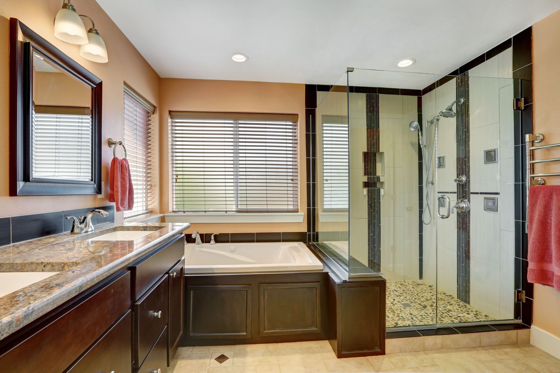 Spacious bathroom with double vanity, window blinds, built-in bench, and glass-enclosed walk-in shower.