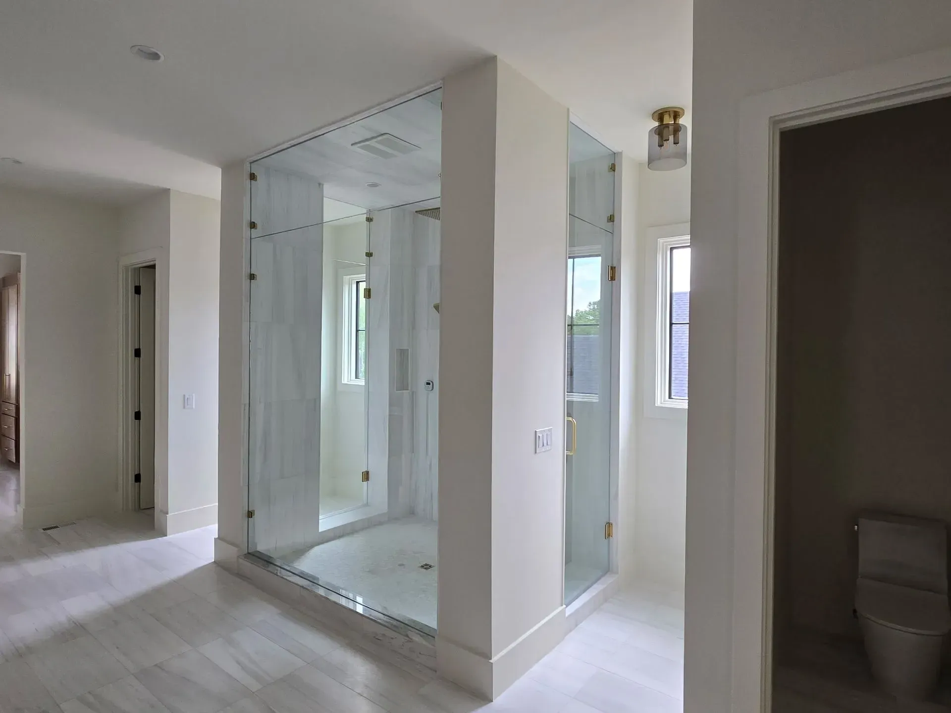 Bright bathroom interior with glass shower, tiled floor, and toilet alcove