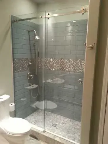 Small bathroom with a glass-enclosed shower, gray tile walls, and a toilet in the foreground.
