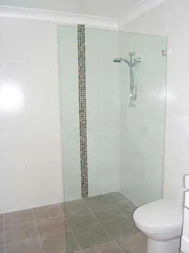 Accessible bathroom shower with glass enclosure, mosaic accent tile, and wall-mounted grab bar beside a toilet