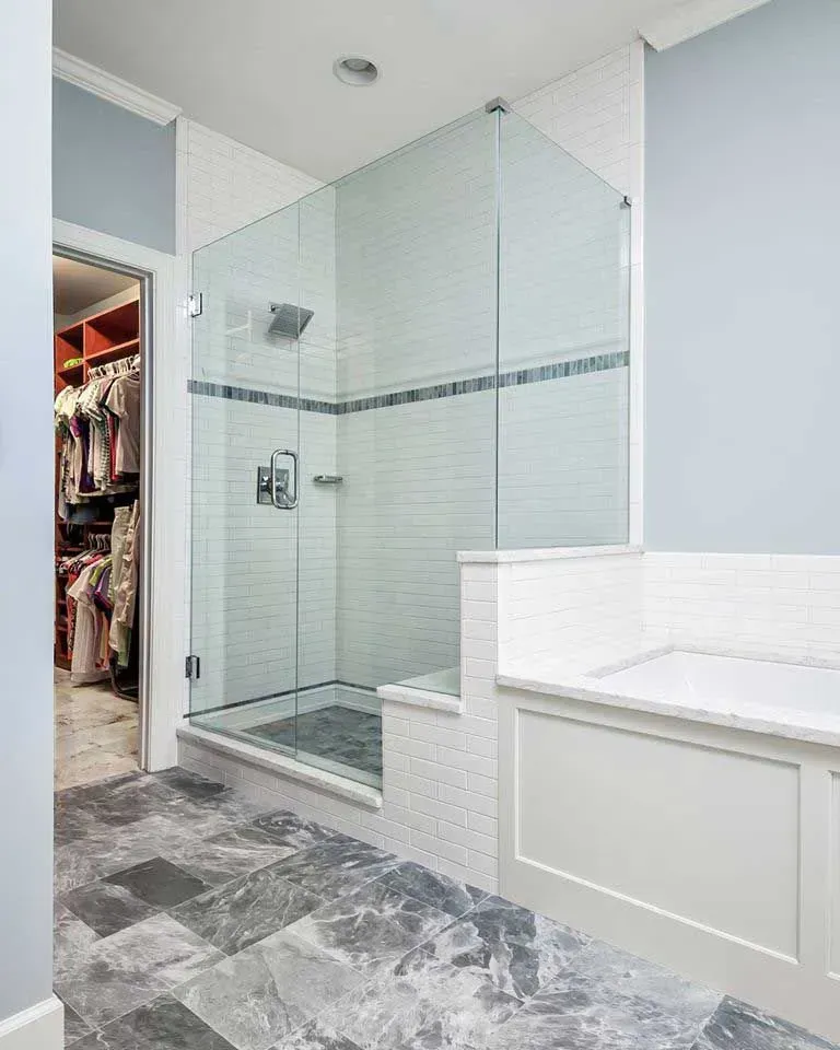 Modern bathroom with a glass walk-in shower and marble tile floor, next to a white vanity.