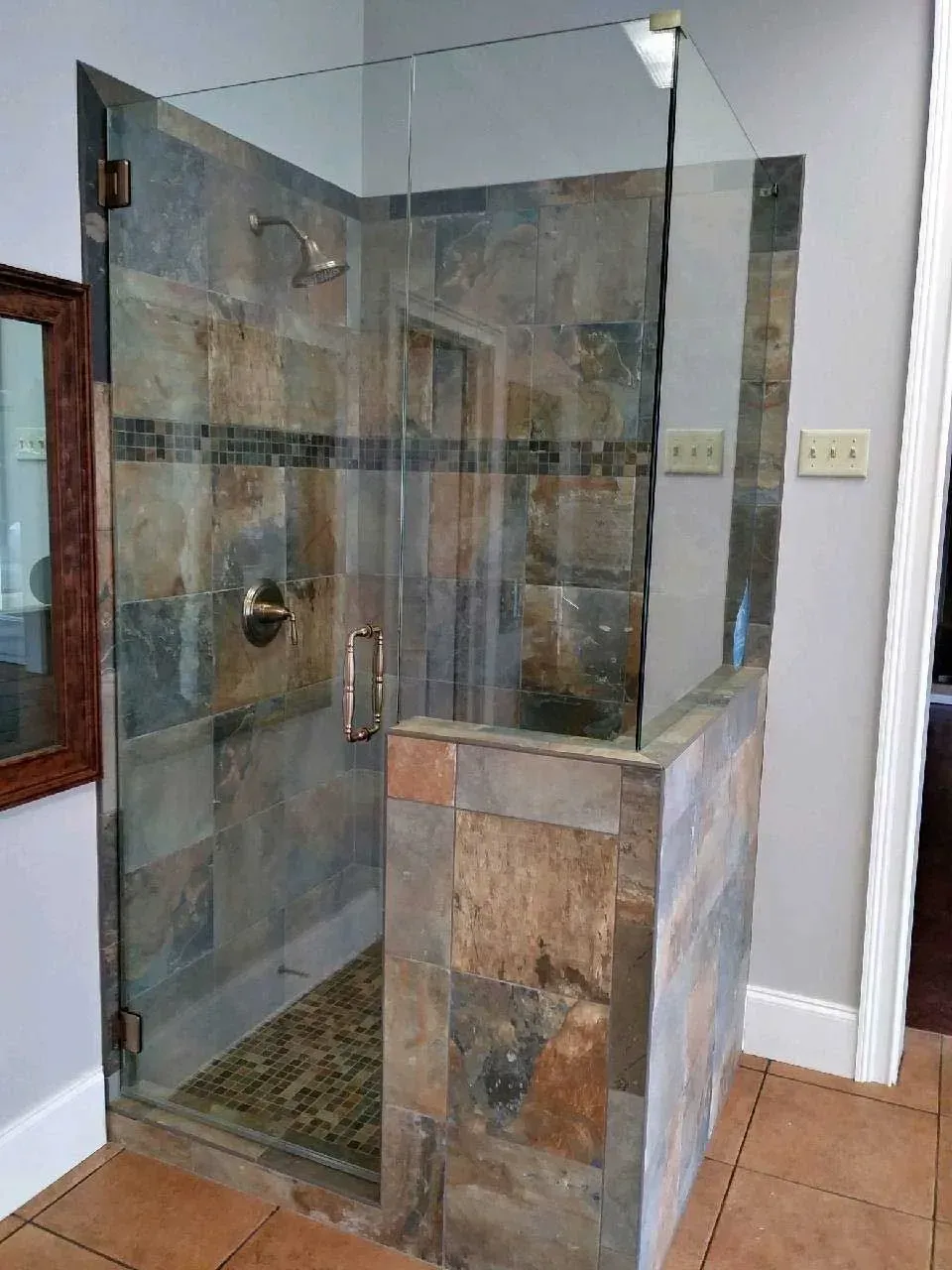 Glass walk-in shower with stone tile walls and a tiled half wall in a bathroom