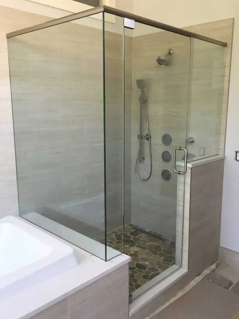 Glass walk-in shower with chrome fixtures beside a white bathtub and tiled floor.