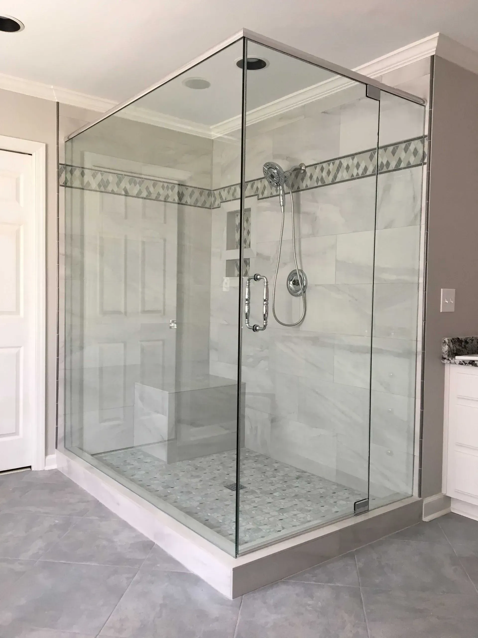 Modern glass-enclosed walk-in shower in a tiled bathroom with marble-look walls and floor.