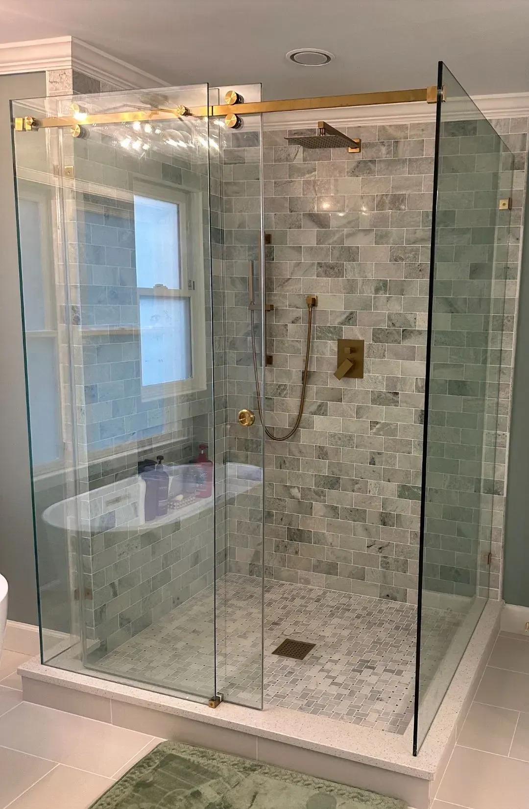 Glass-enclosed tiled shower with brass fixtures in a bright white bathroom