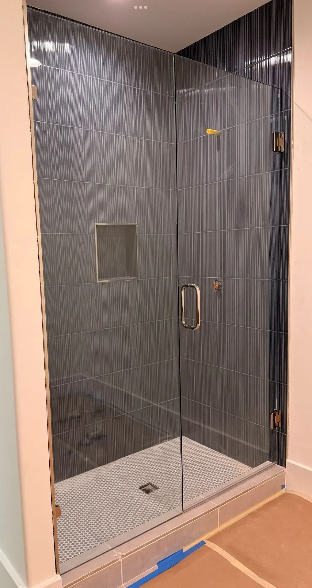 Glass shower enclosure with dark gray tiled walls and a tiled floor in a bathroom