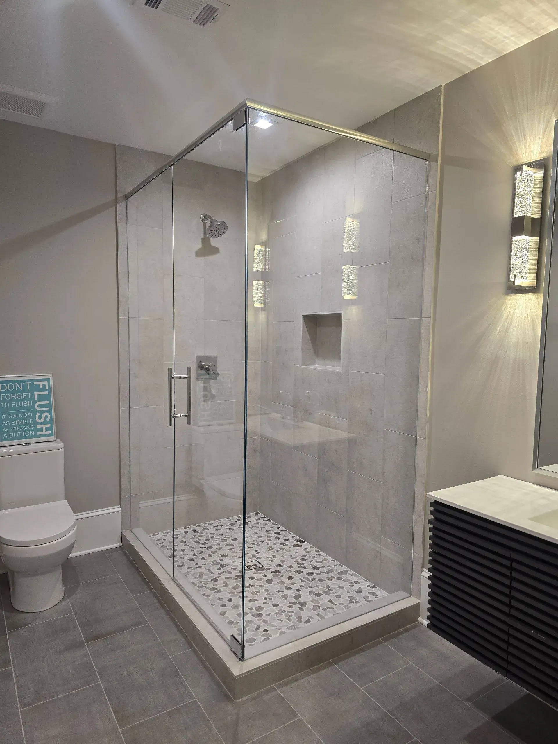 Modern bathroom with a glass walk-in shower, toilet, and wall sconces on gray walls