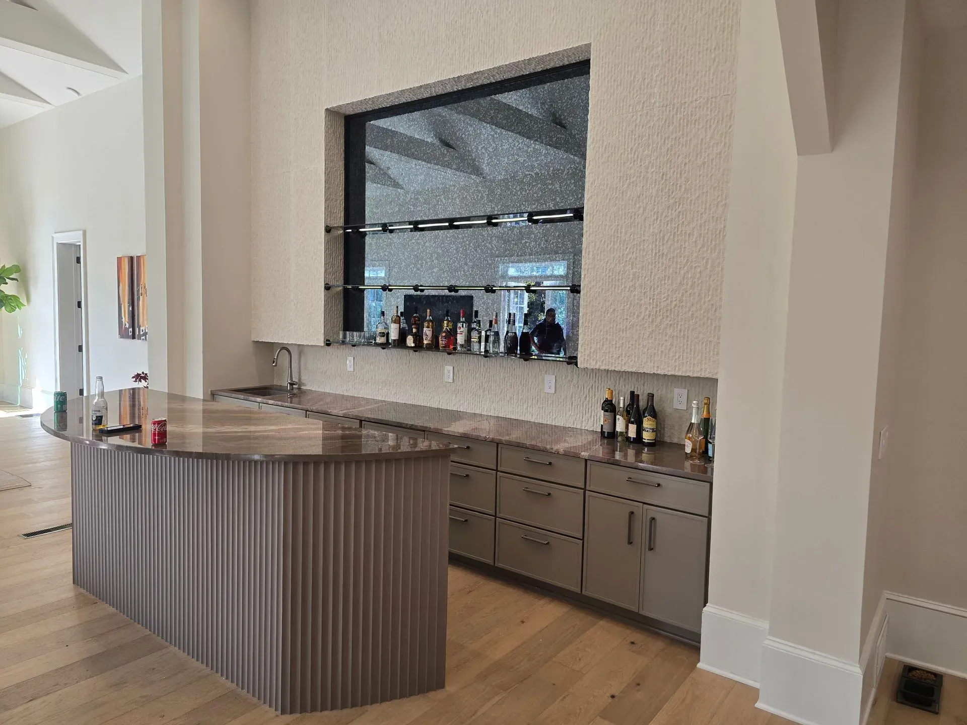 Modern kitchen with a curved wood island, built-in bar, and a large wall mirror reflecting the room.