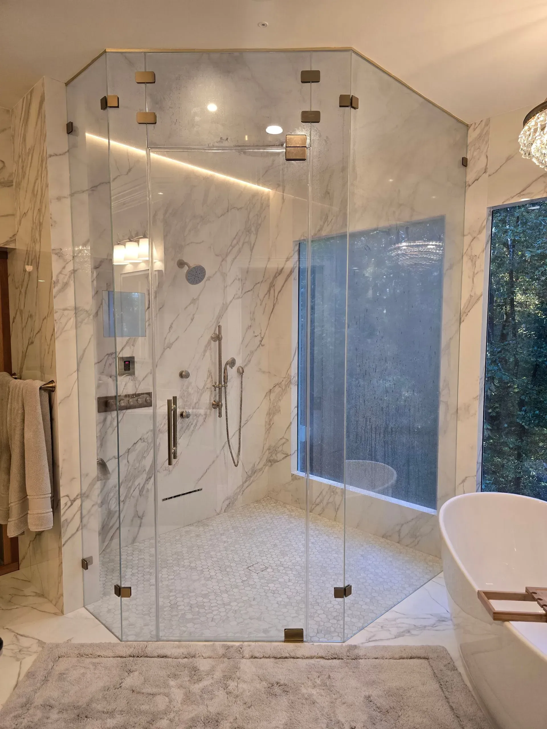 Glass shower enclosure in a marble bathroom with blue-tiled wall and freestanding tub