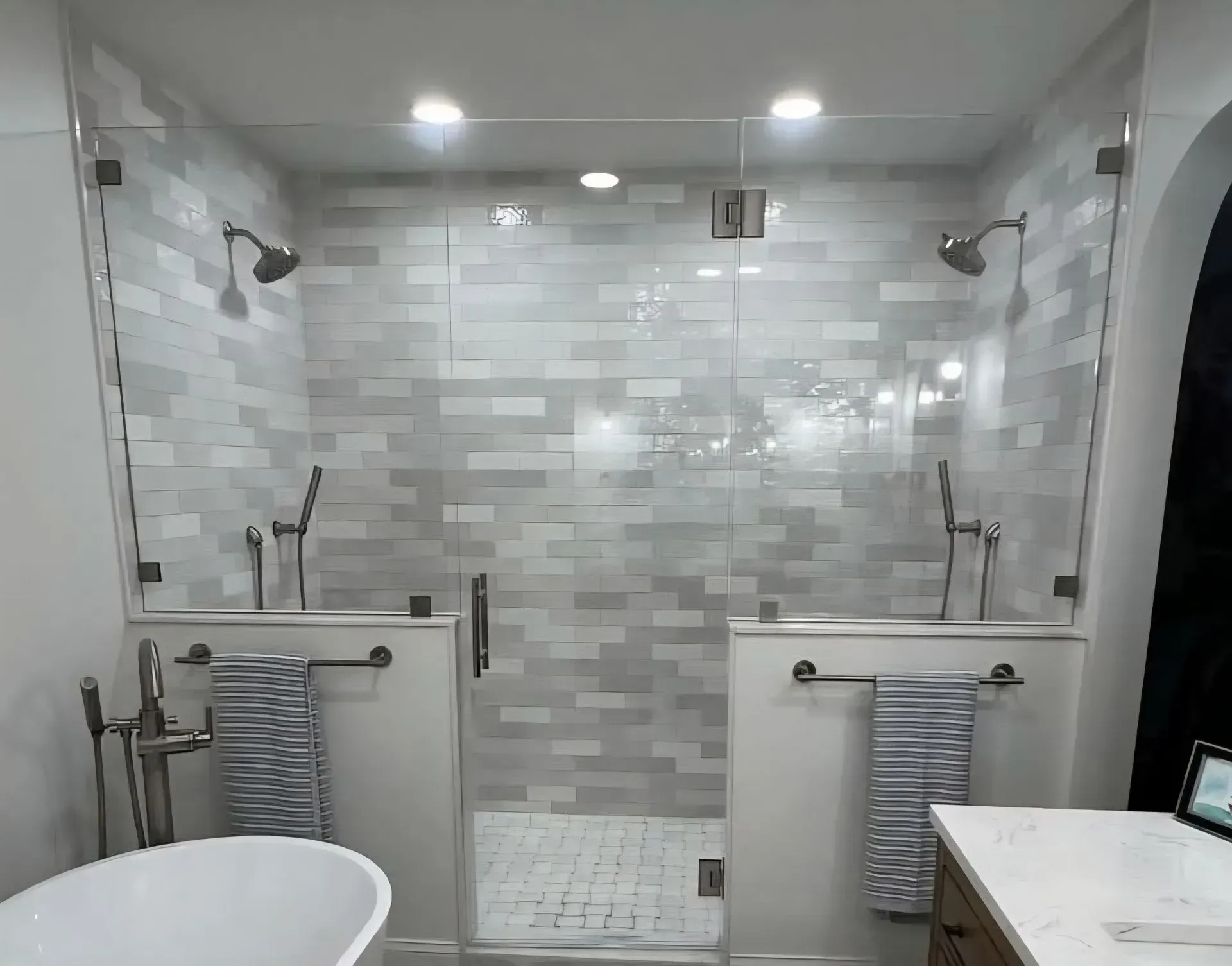 Accessible walk-in shower with gray tile, glass doors, and built-in bench in a bright bathroom