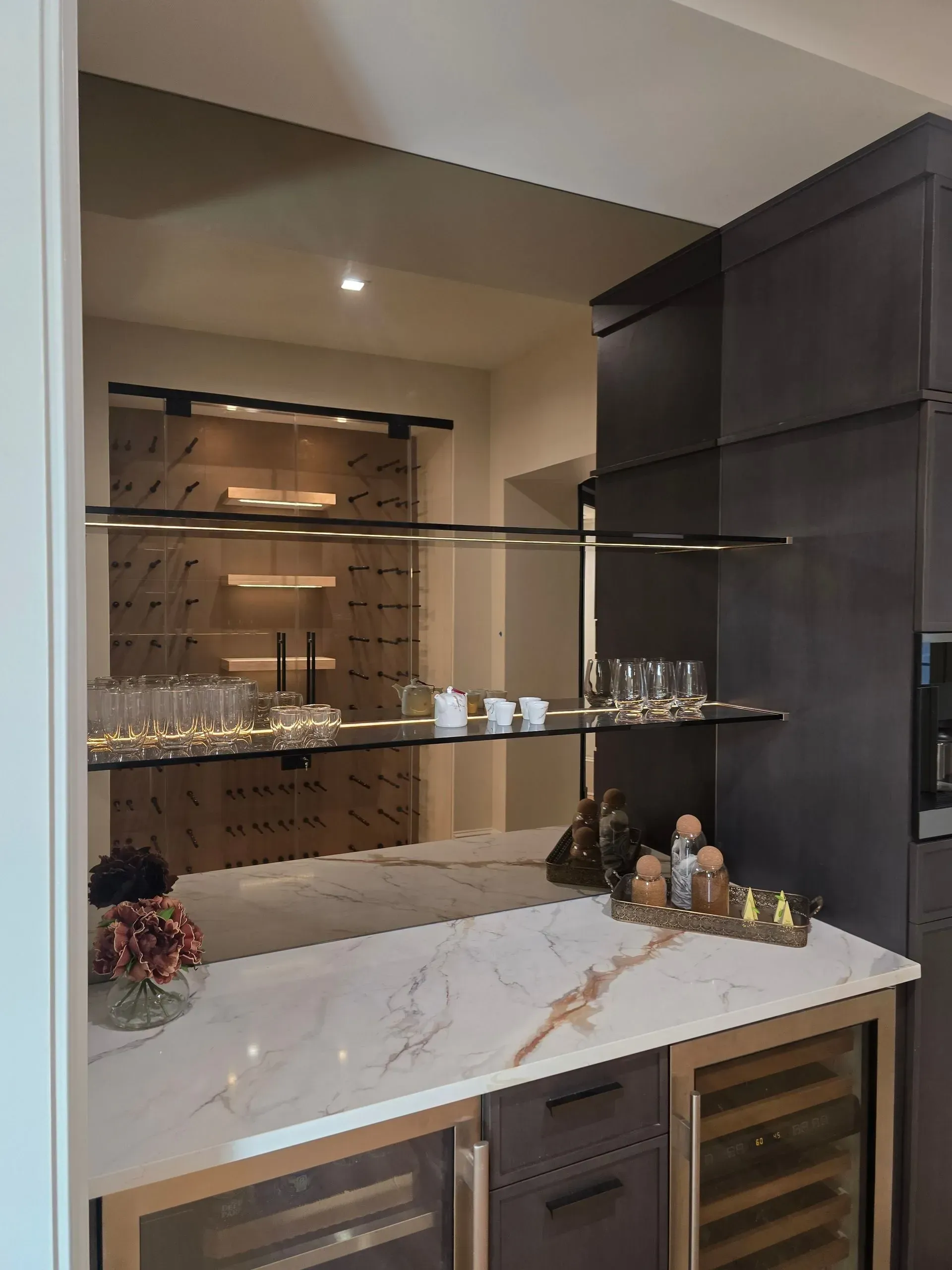 Modern built-in bar cabinet with marble counter, glassware, and dark wood shelving in a home interior