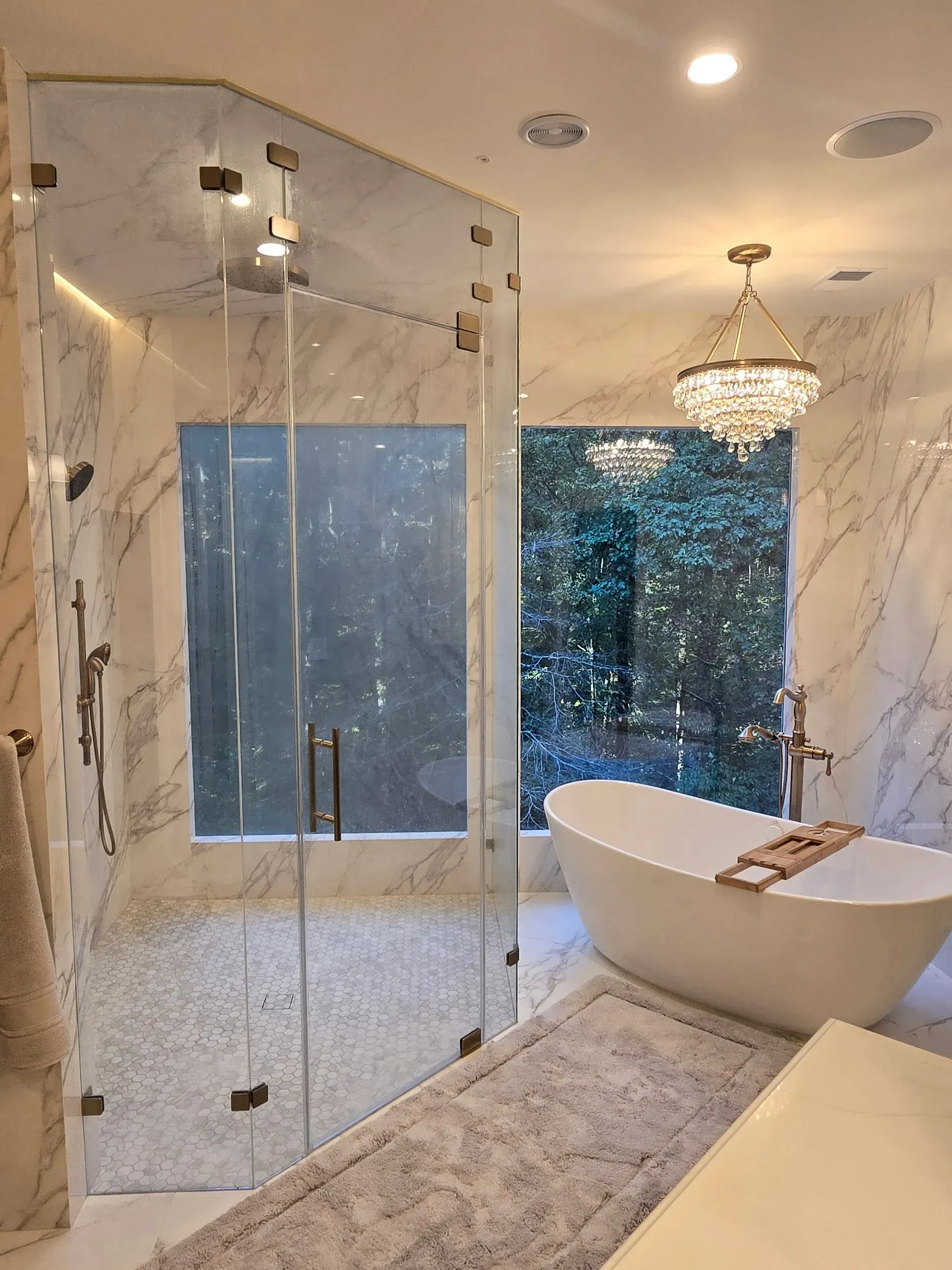 Luxurious bathroom with glass shower, freestanding tub, chandelier, and marble finishes