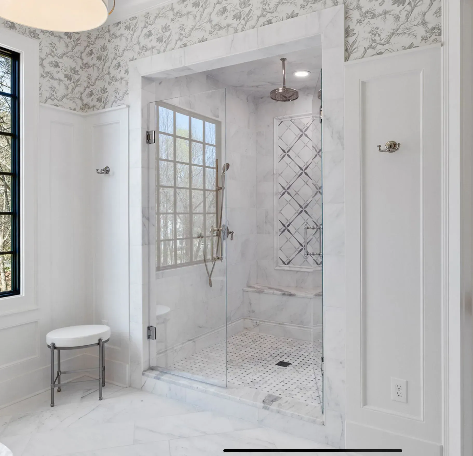 Bright white bathroom with glass shower enclosure, marble tile, and wallpapered walls