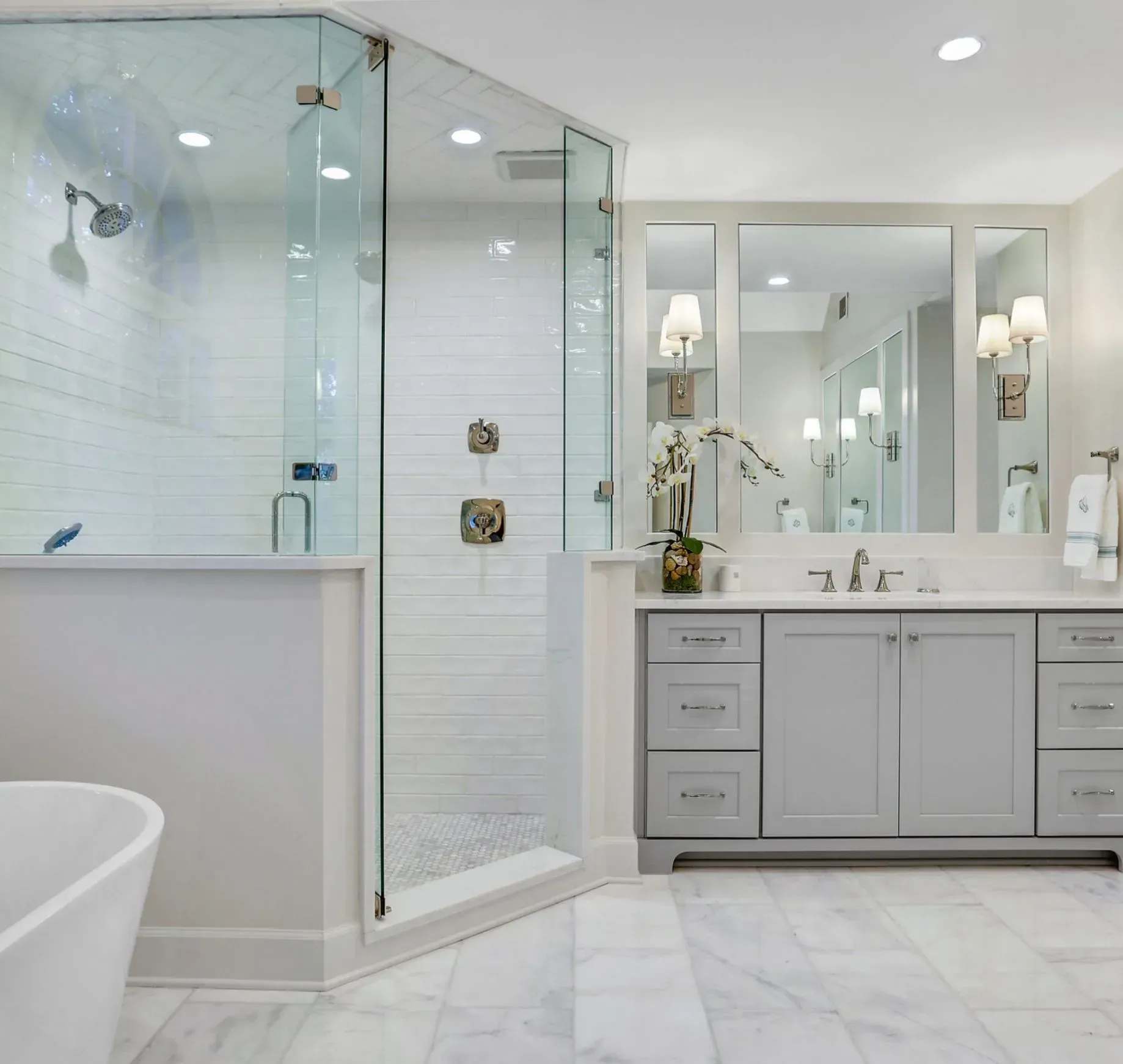 Bright modern bathroom with glass shower, freestanding tub, double vanity, and white marble-style tile.