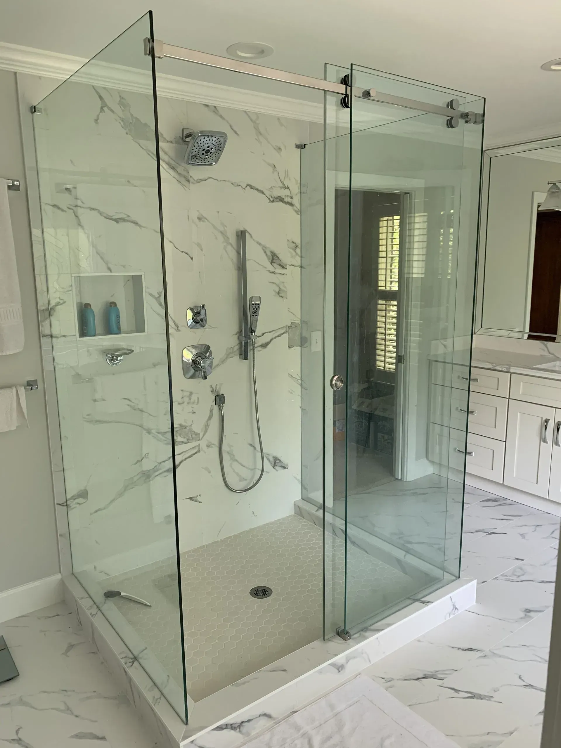 Glass shower enclosure in a bright marble bathroom with tiled floor and chrome fixtures
