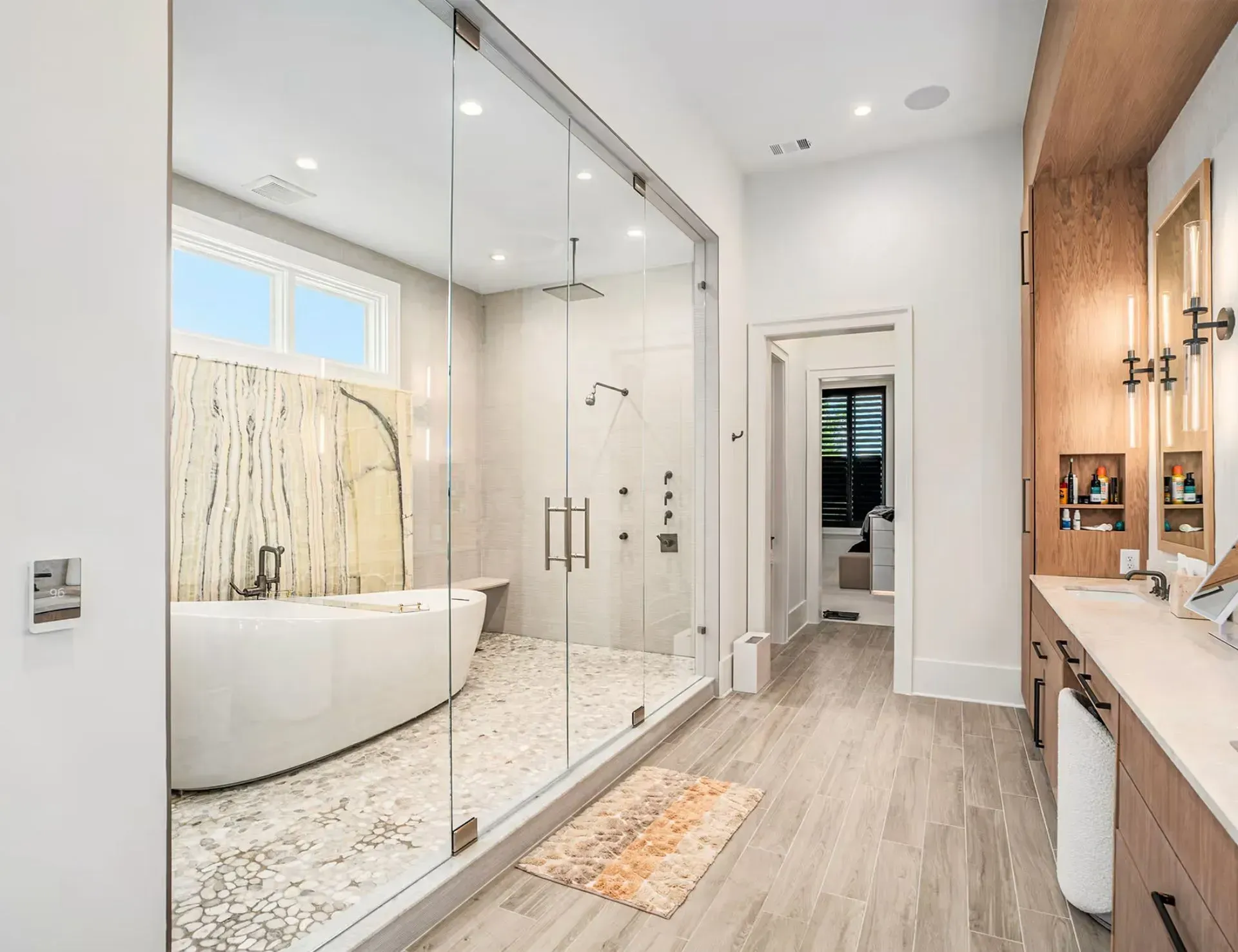 Modern bathroom with glass shower, freestanding tub, double vanity, and light wood flooring