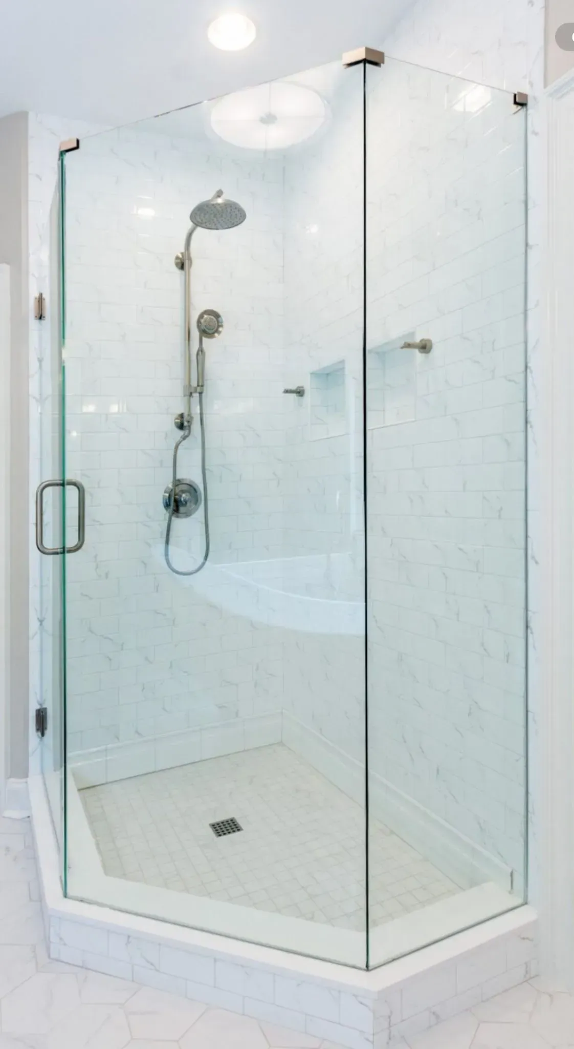 Corner glass shower with white tile, chrome showerhead, and built-in shower bench
