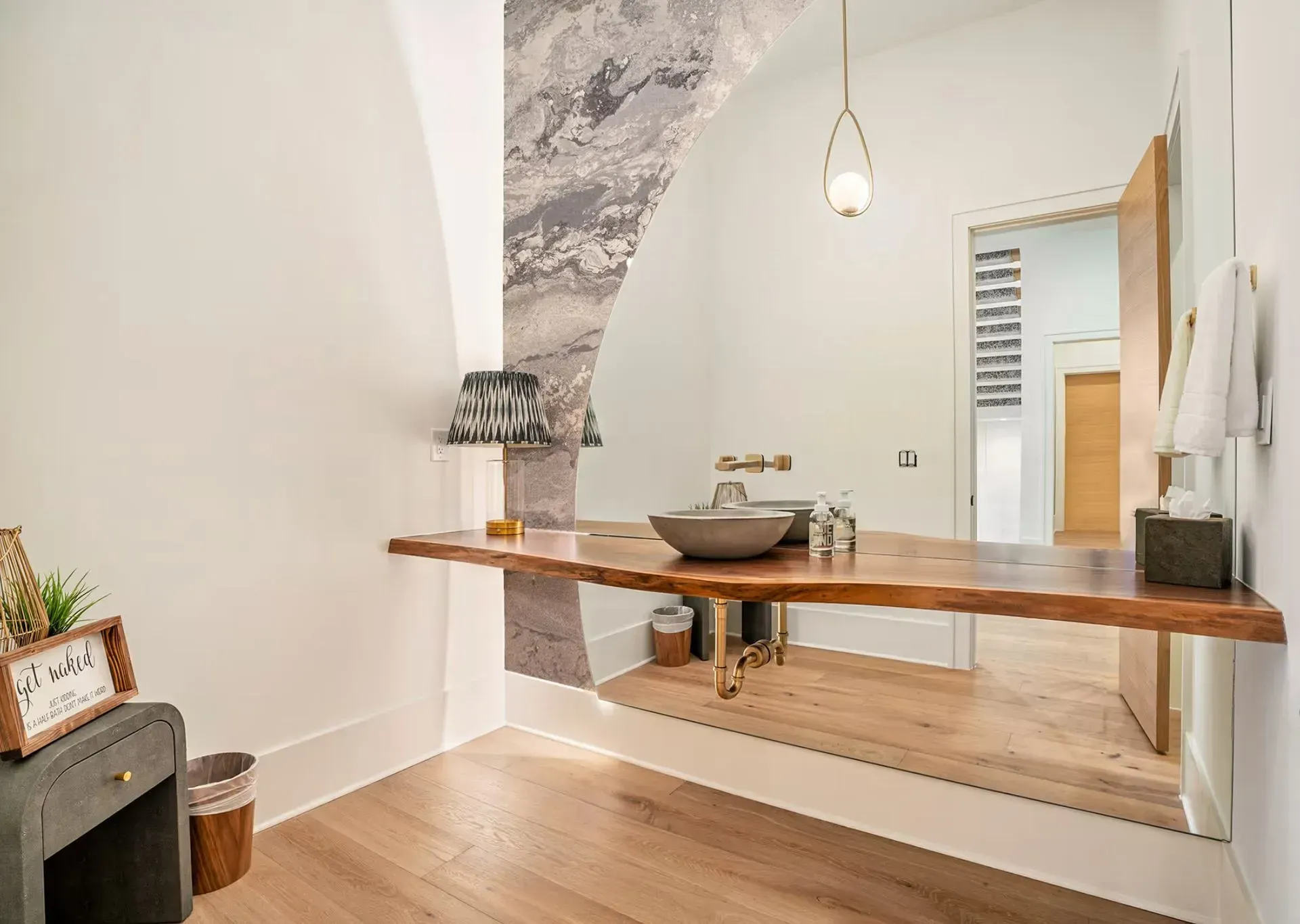 Modern bathroom with a floating wood vanity, round sink, and large mirror under a hanging light.